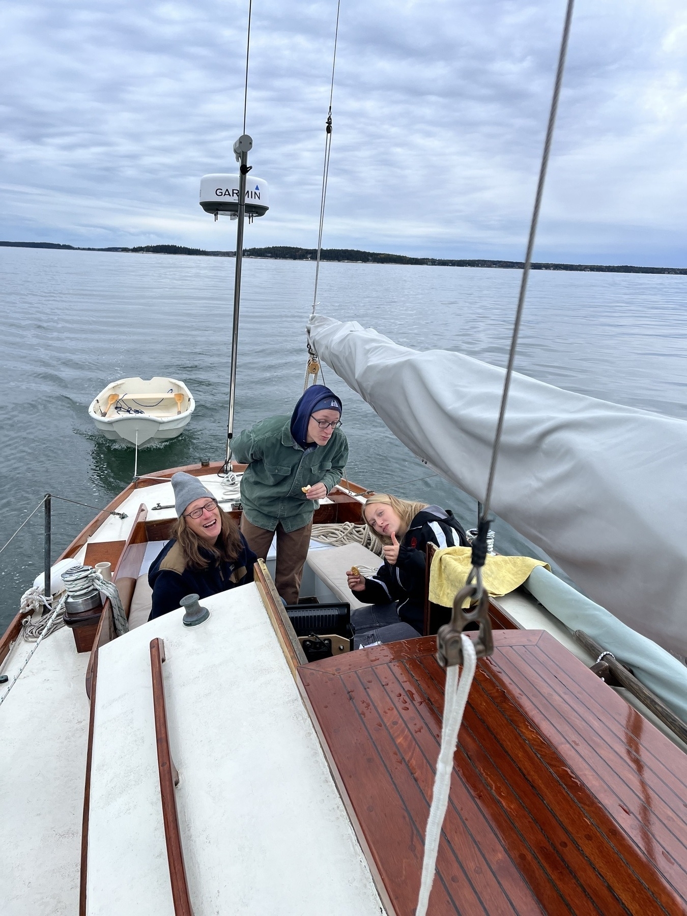 Three people in the cockpit of a 30’sailboat motoring. Gray water and gray sky. 