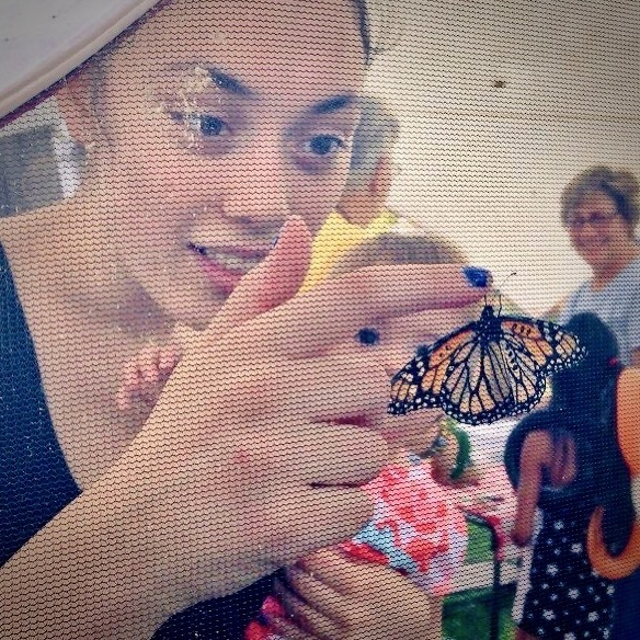 Woman holding infant and touching Monarch butterfly in a butterfly tent at a festival.