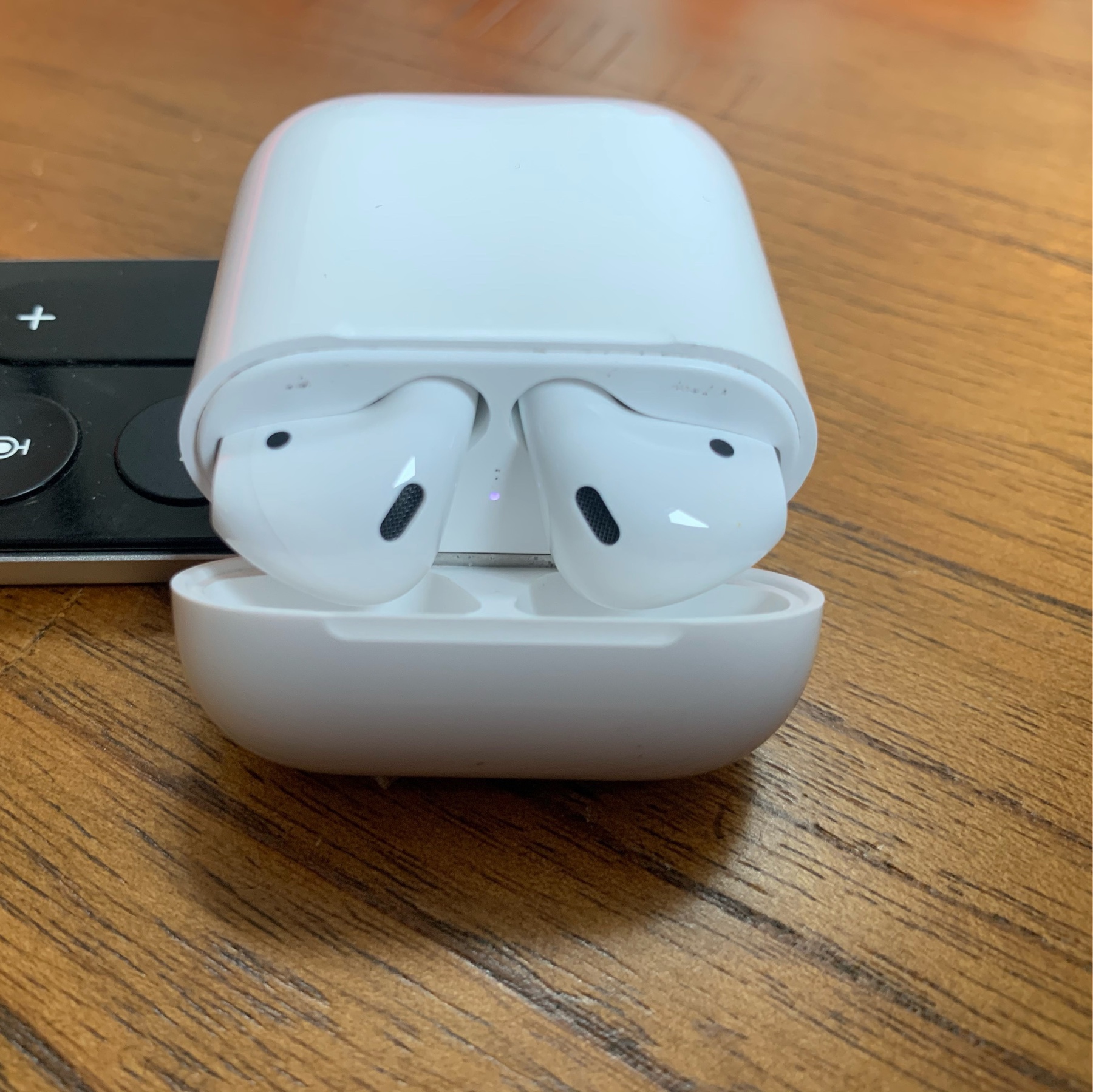 My brand new Airpods (second gen) in my original charging case, sitting open on a wooden table.