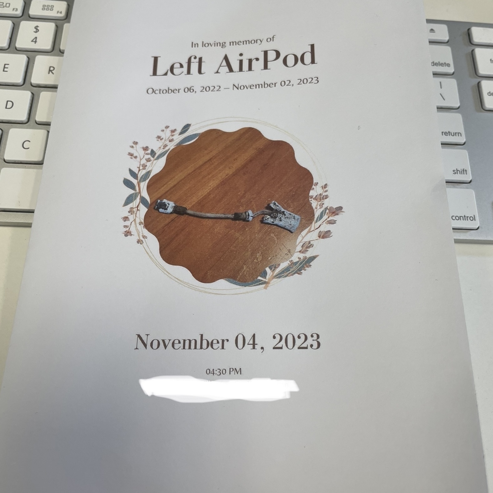 The memorial card for my left AirPod, as left in my desk. a card with a contred photo of my crished left AirPod and the words "In loving memory of Left AirPod October 06, 2022 - November 02, 2023"