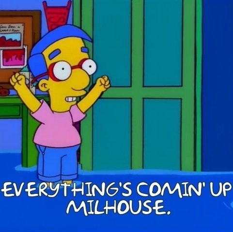 A screenshot from The Simpsons. Milhouse is standing in water, his feet are submerged. but the cuffs f his trouser legs are above the water line. His arms are raised in triumph. The image is subtitled with his words "Everything's coming up Milhouse!"