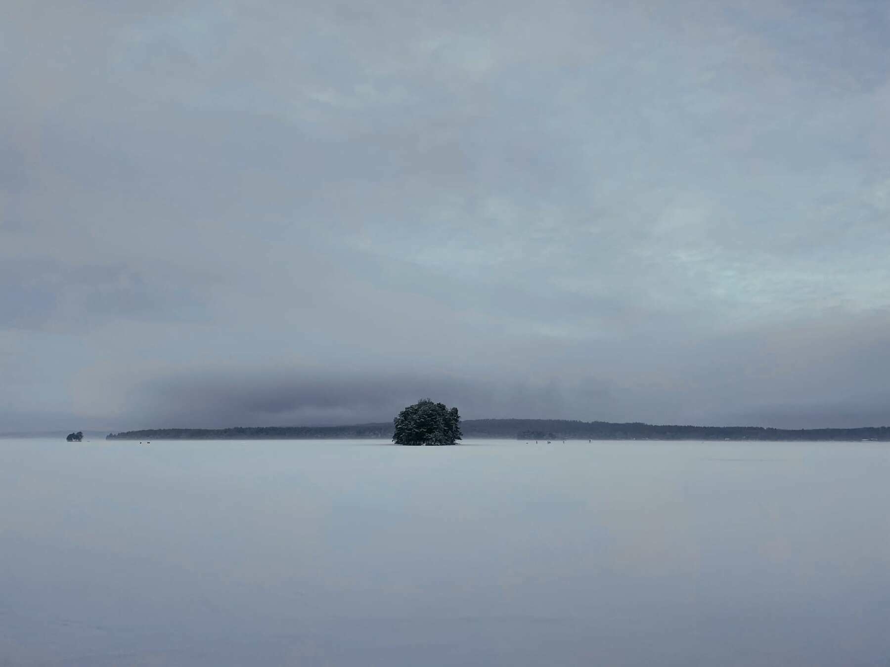 A frozen lake and overcast sky. Tiny looking humans can be spotted in the far distance.
