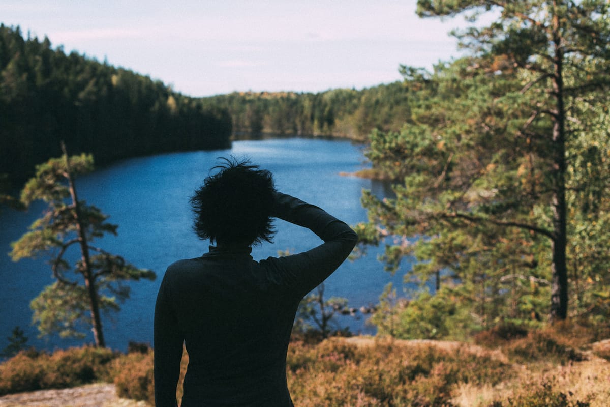 A woman looks out over a lake surrounded by a lush green forest.