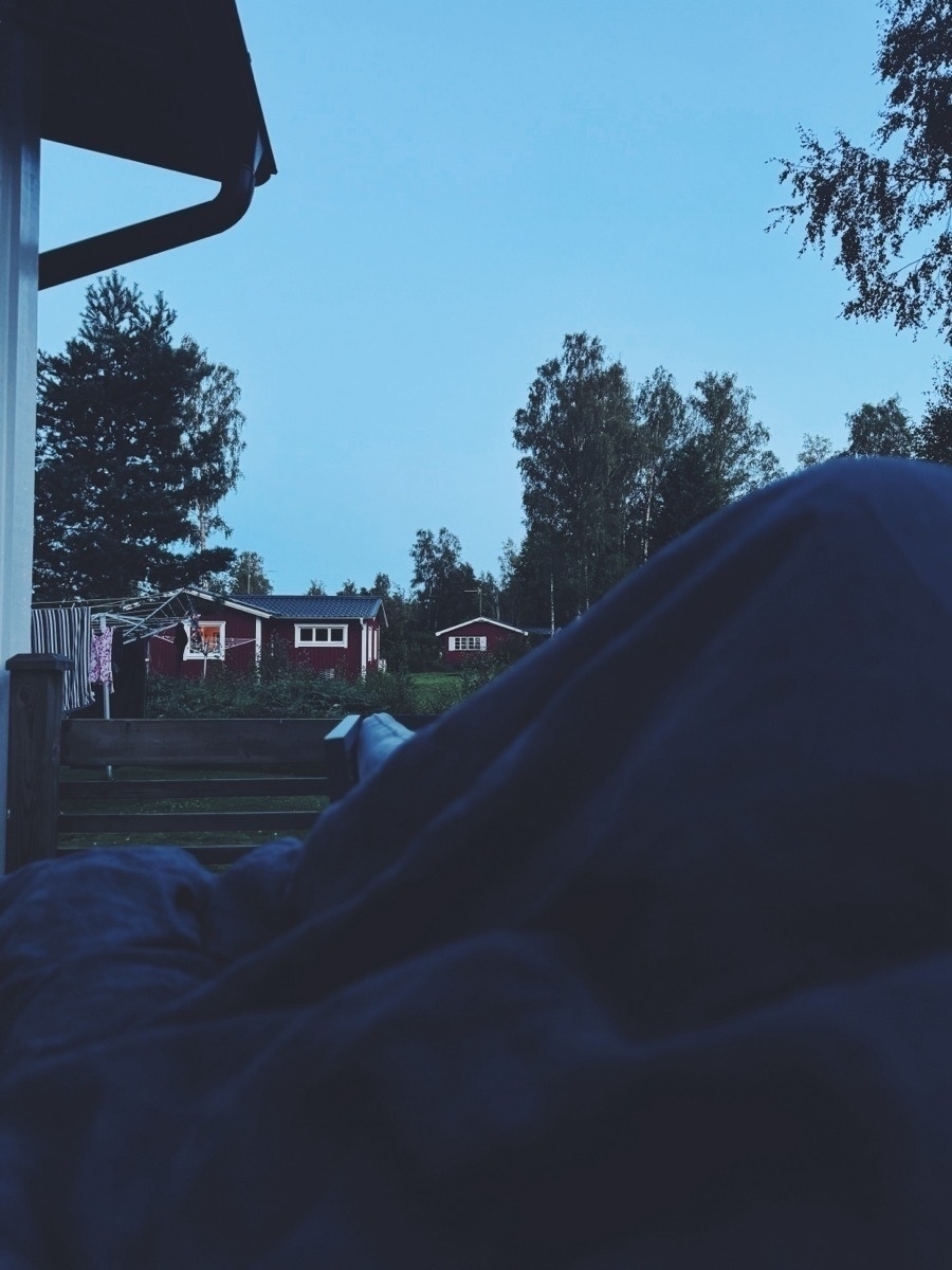 Tucked under cozy blankets, gazing at a tranquil evening sky over red cabins and trees.