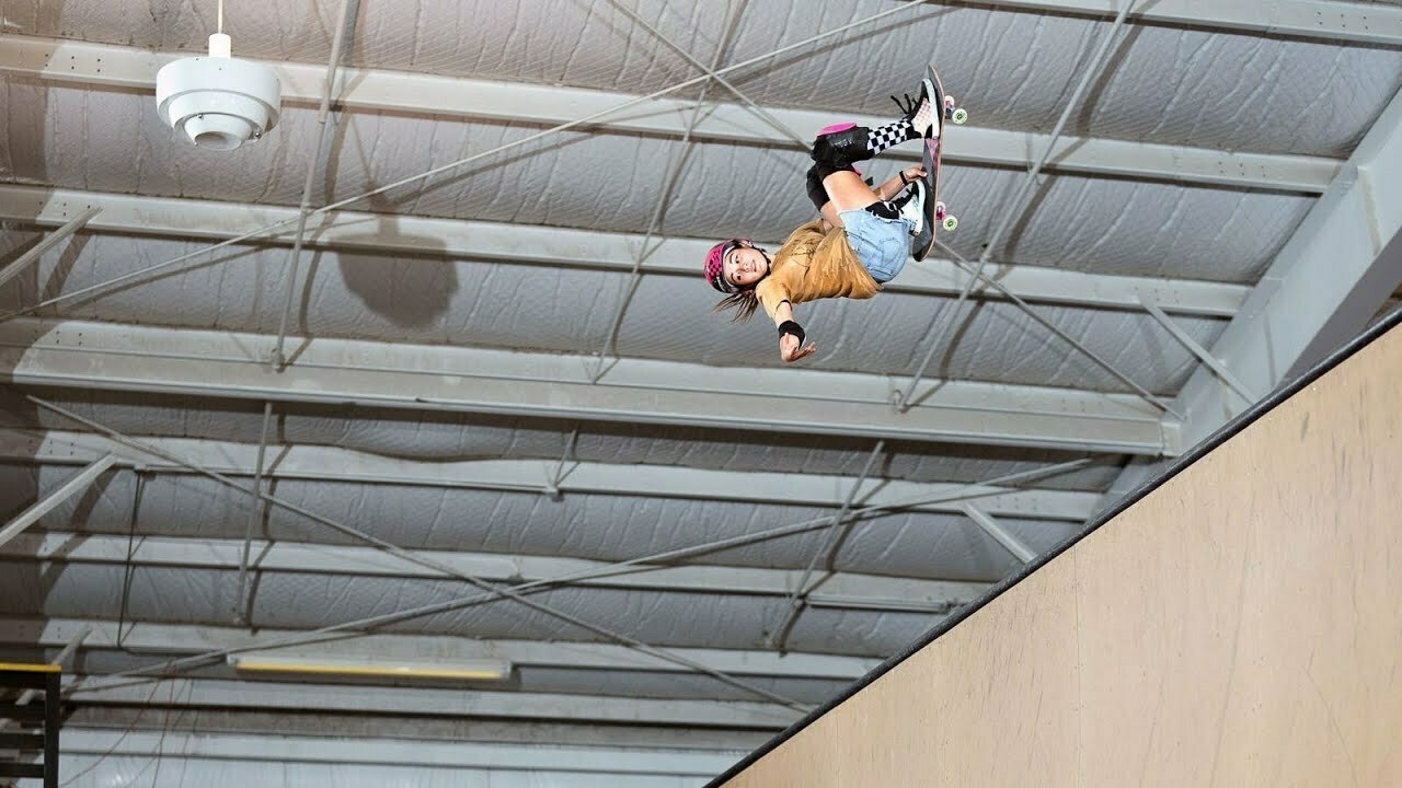 Arisa in the air, performing the 900 above a skate ramp in an indoor park.