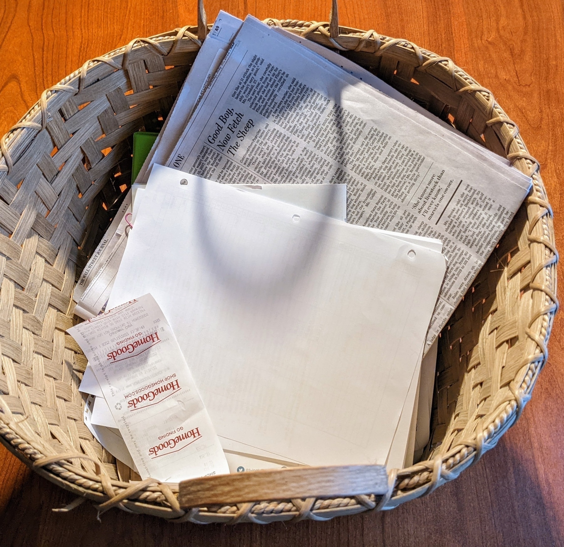 wooden basket containing a pile of paper, including a receipt, a handout, and a newspaper section
