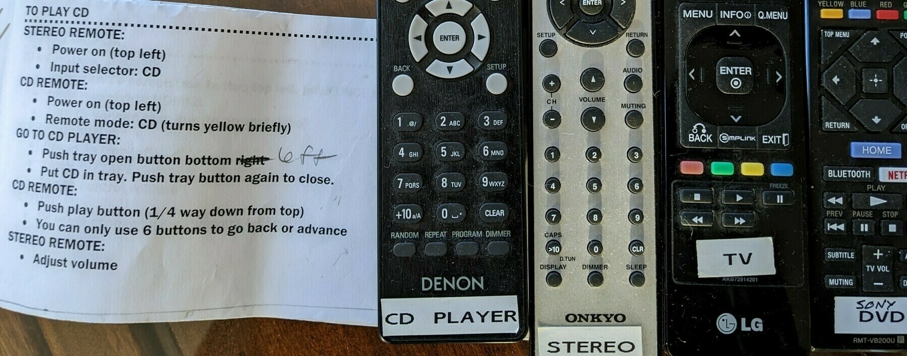 a small printed book of written instructions next to four remote control devices, labeled CD player, stereo, TV and DVD