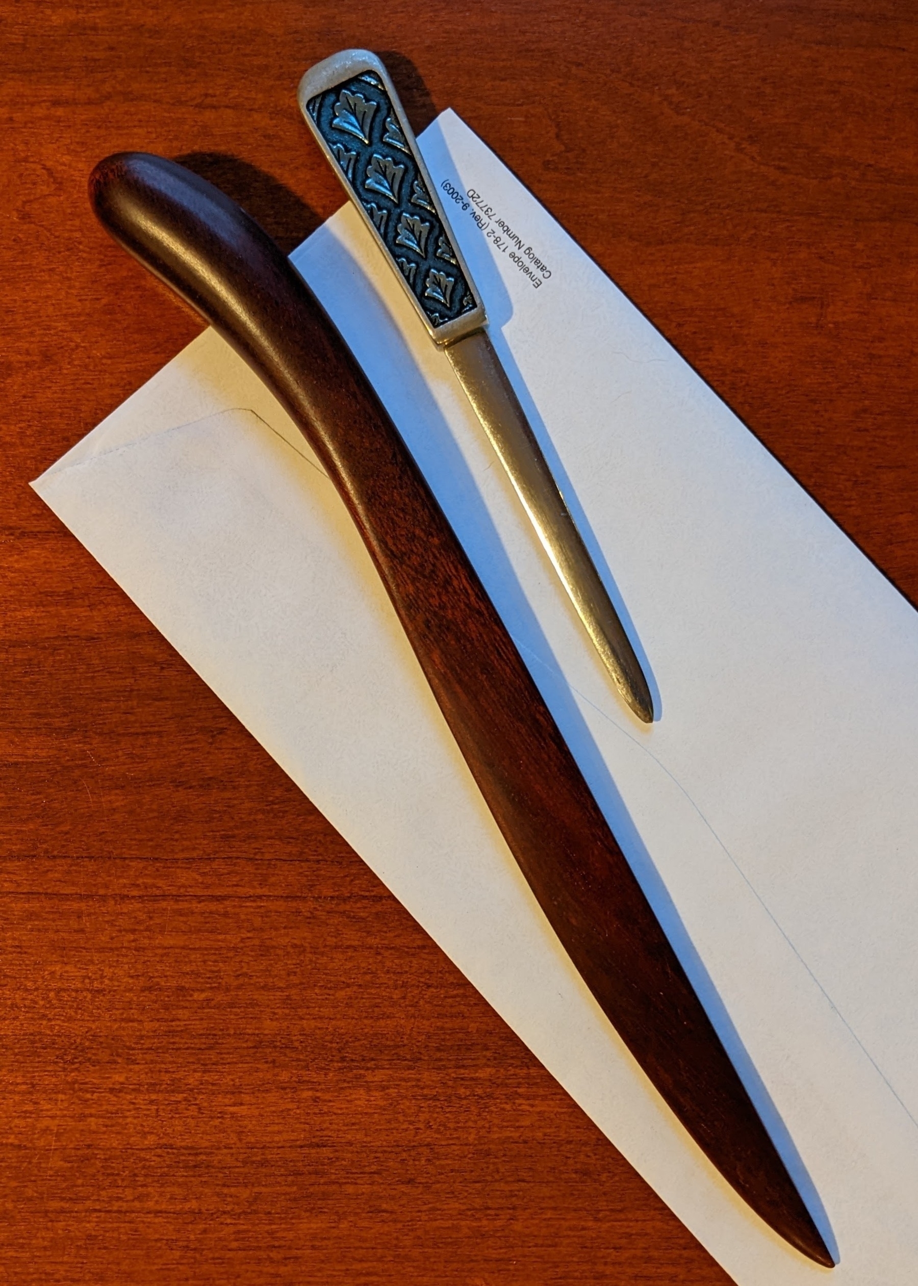 carved wooden letter opener and enameled pewter letter opener resting on top of an envelope