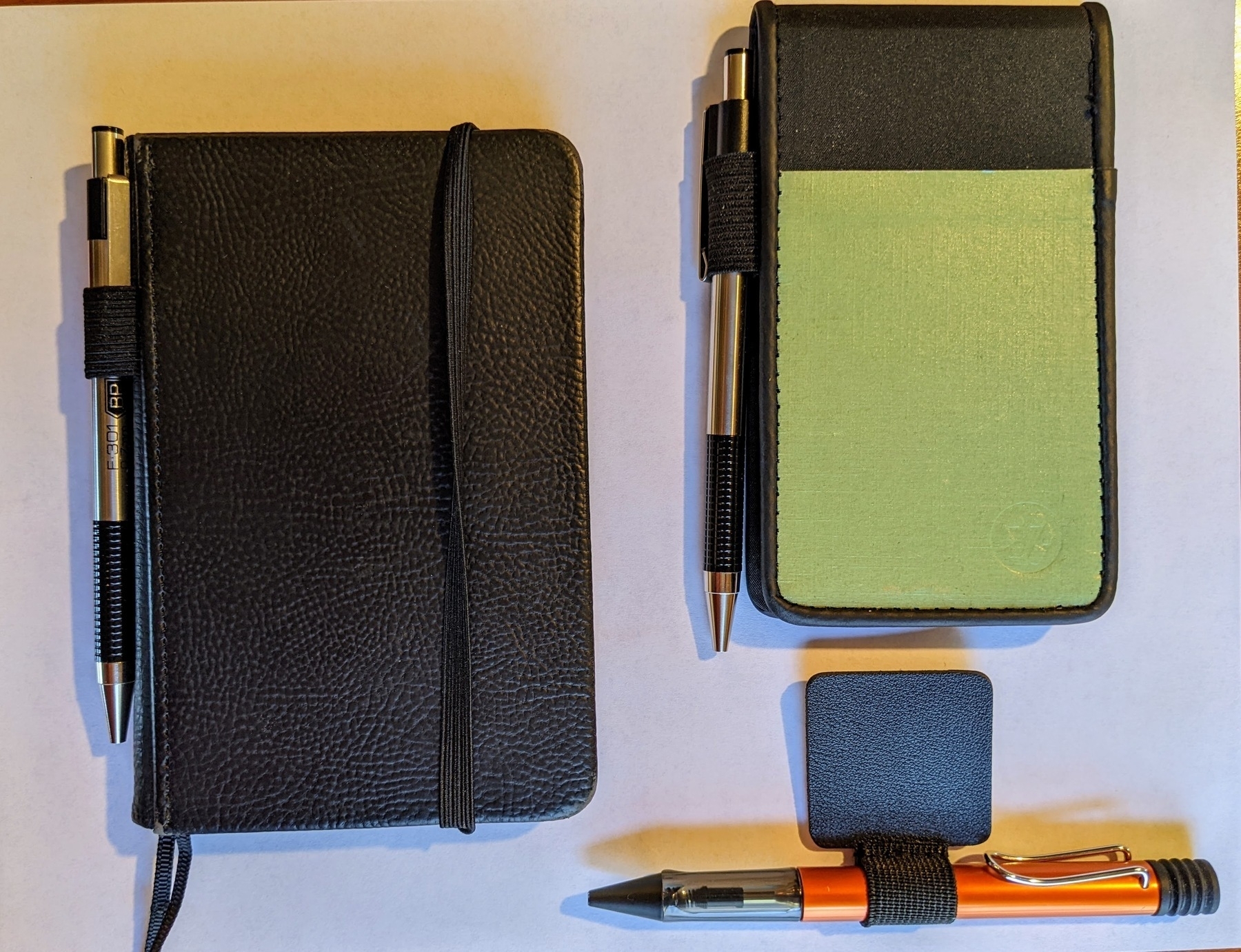 two pocket notebooks with different pen loops attached, and a free-standing pen loop with a sticky backing