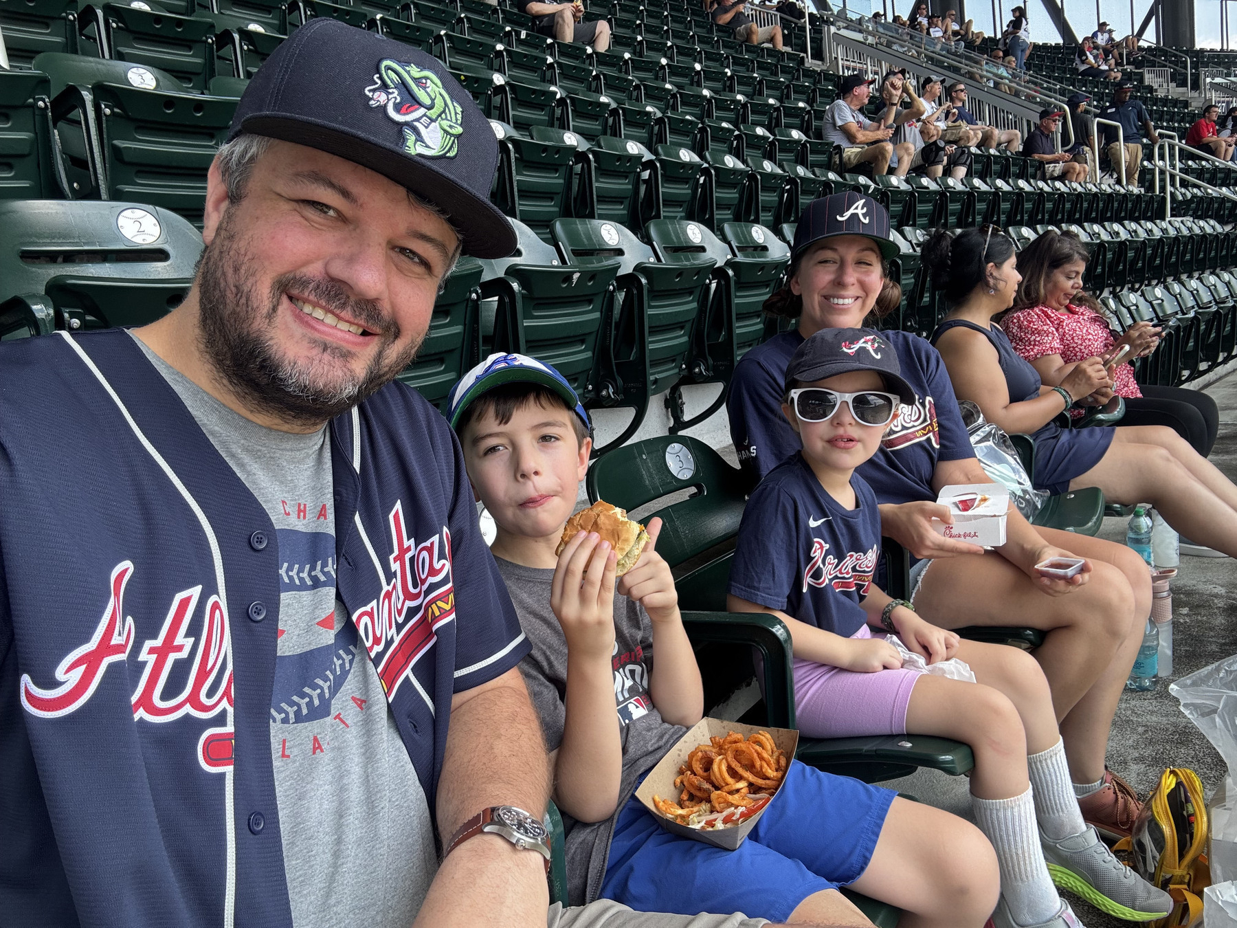 A family is enjoying a day at a baseball game, wearing team jerseys and eating snacks in the stands.