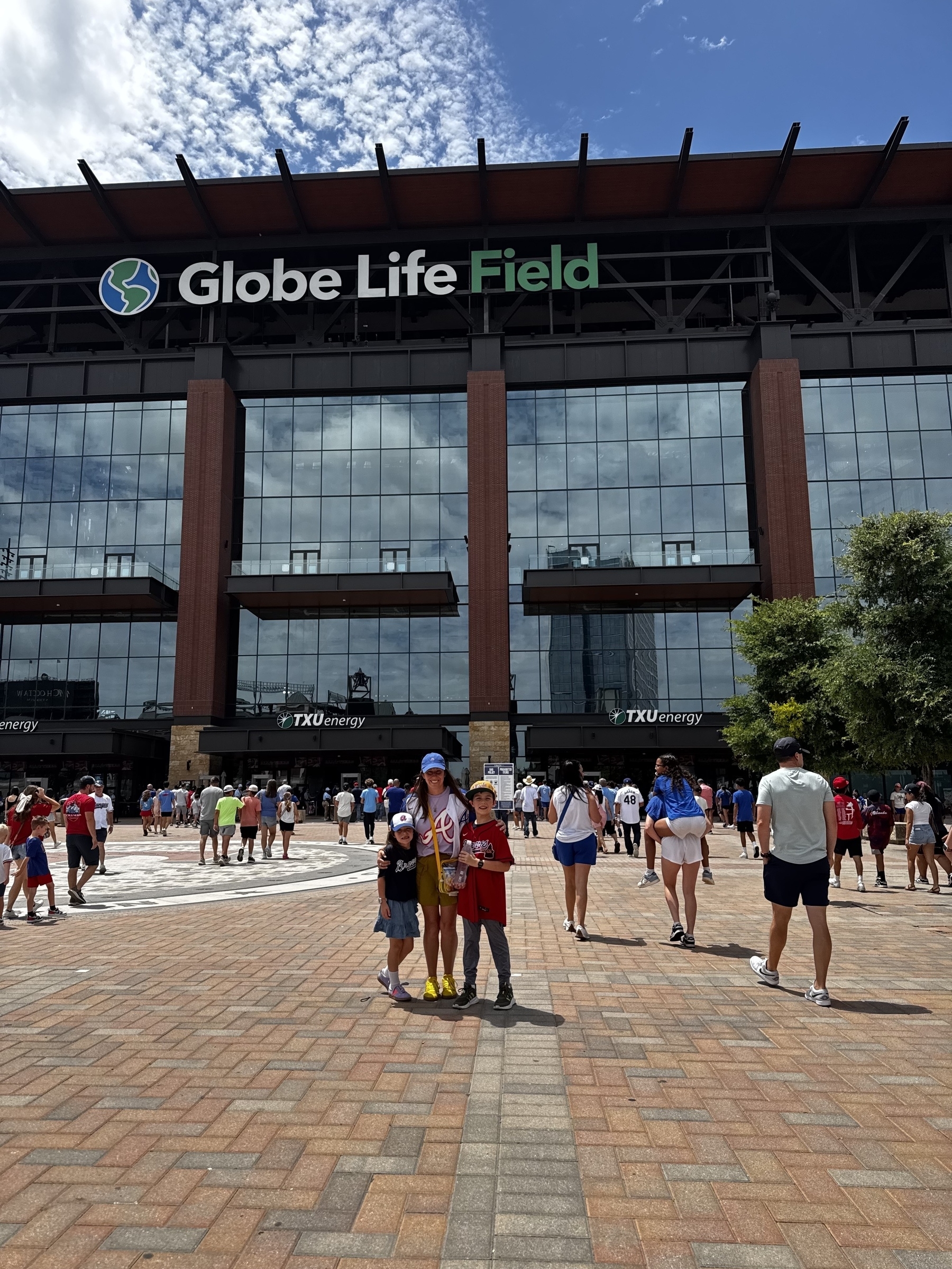 A mother poses with children in front of Globe Life Field, surrounded by people on a sunny day.