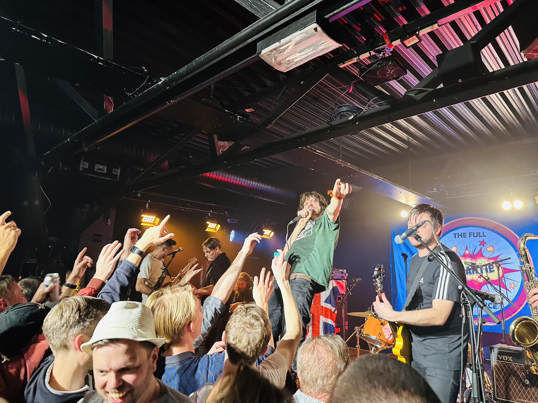 Auto-generated description: A band is performing energetically on stage in front of an enthusiastic crowd at a live concert.