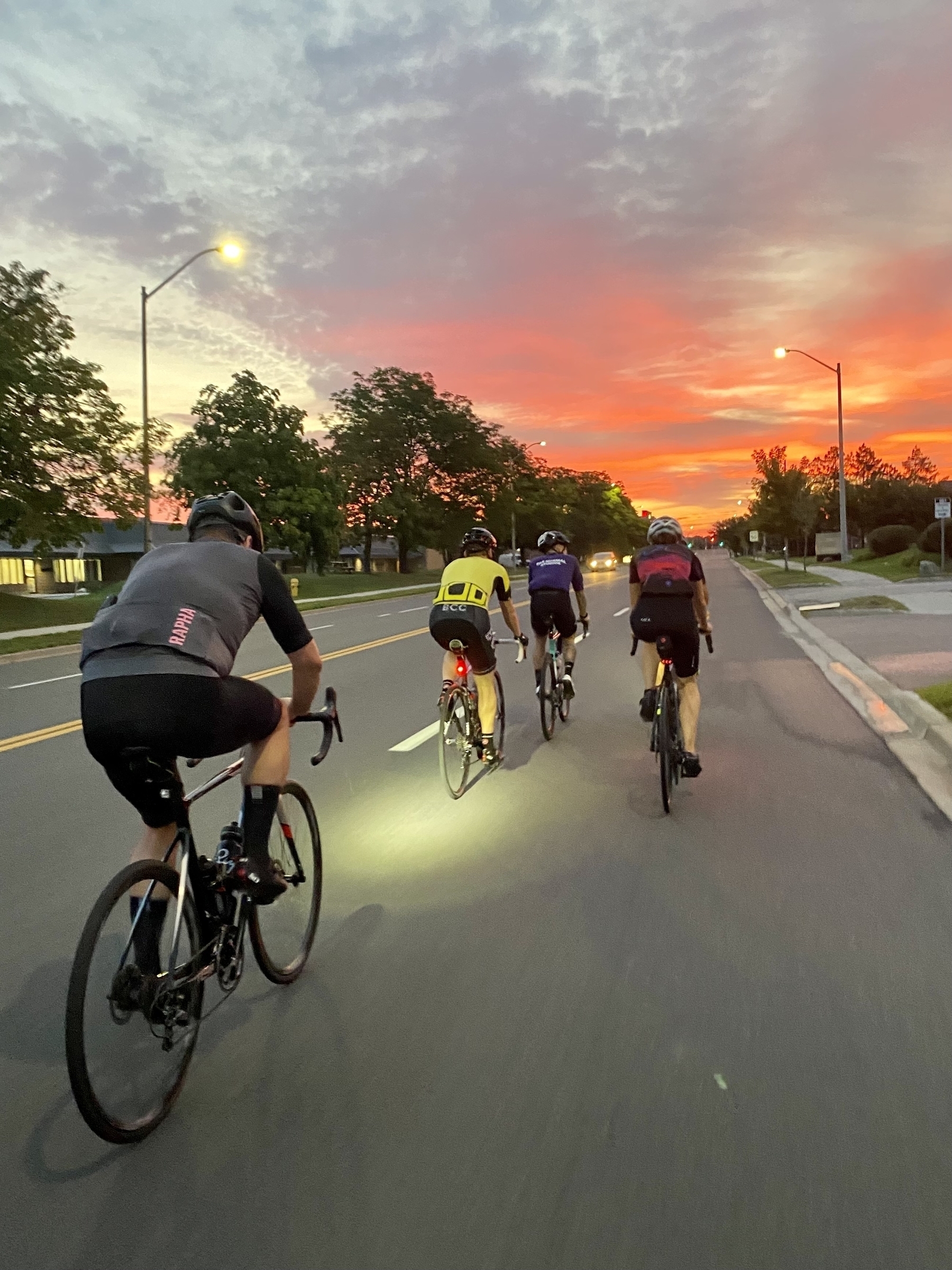 Cyclists riding towards an orange sunrise