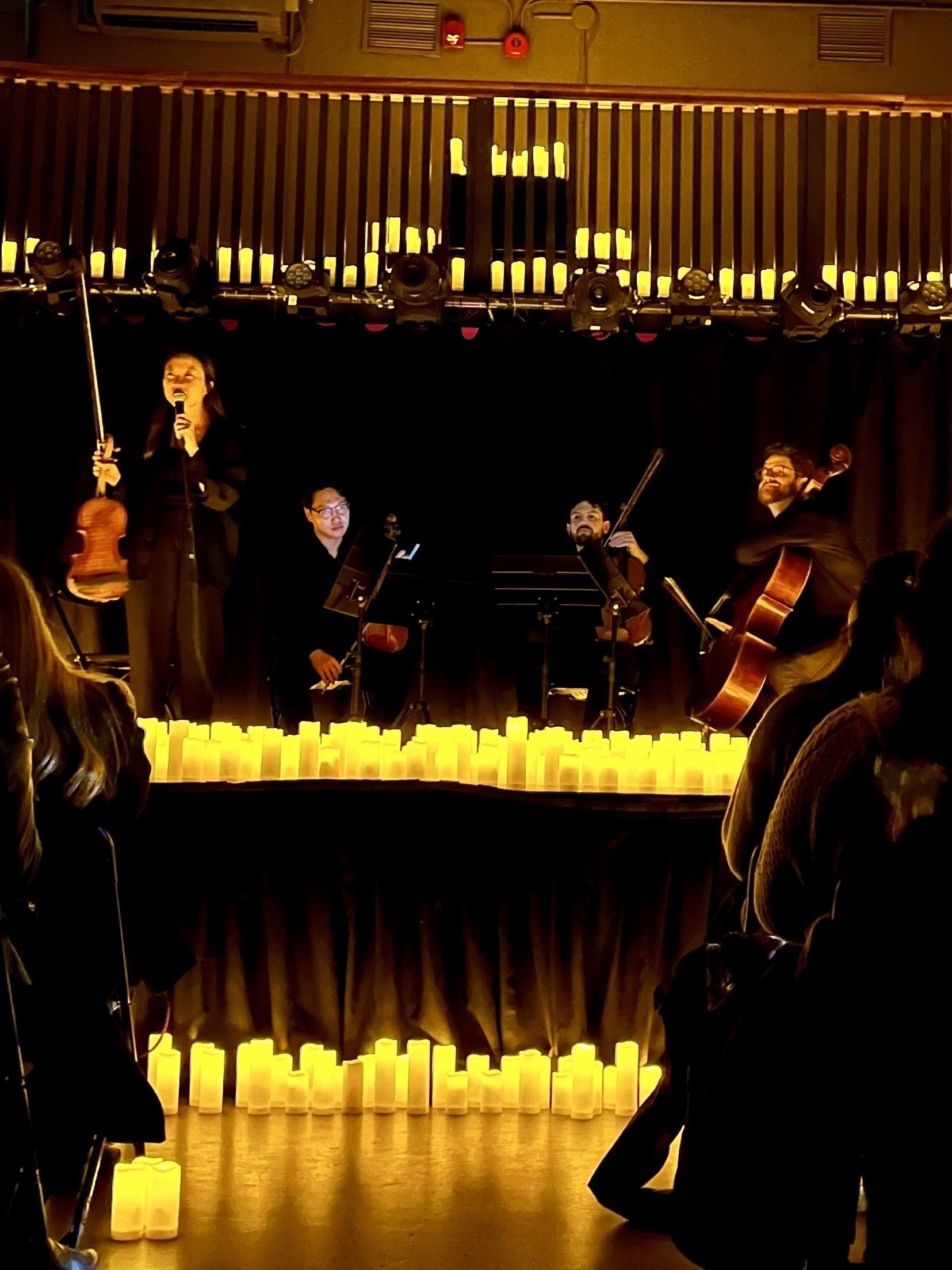 A string quartet up on stage holding their instruments while surrounded by candles