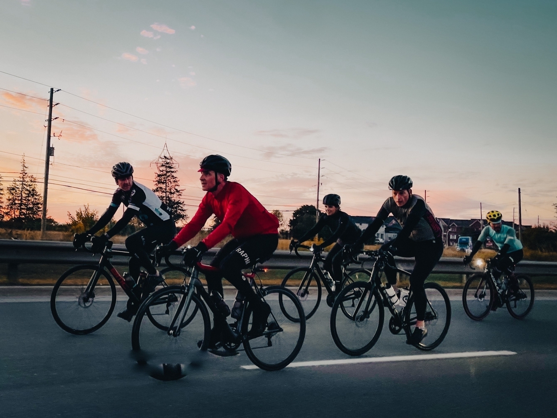 Four cyclists on a road with pink sunrise sky