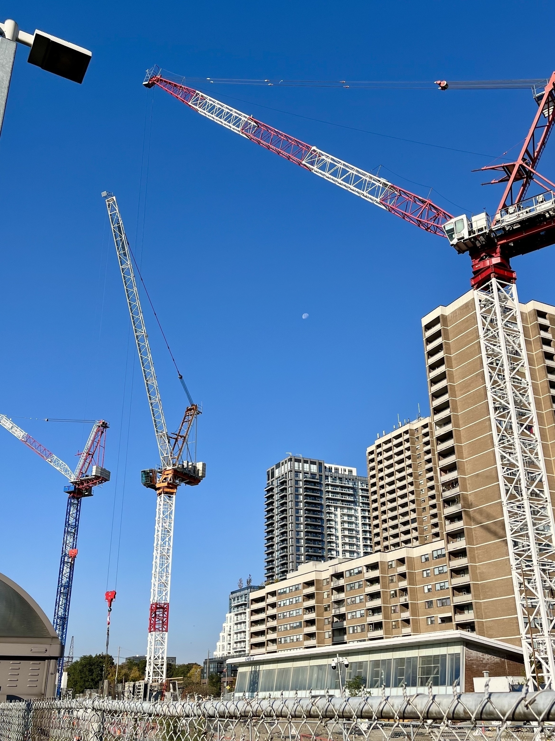 Several tall cranes are positioned around high-rise buildings under a clear blue sky.