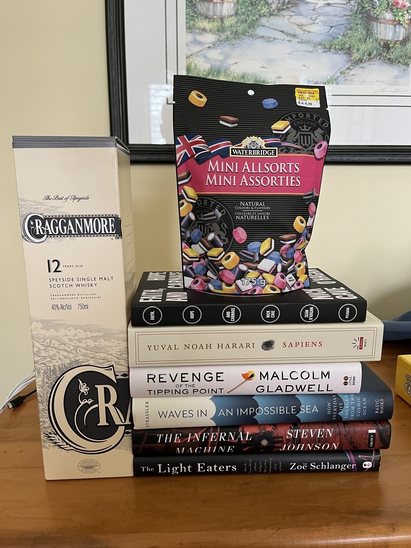 A collection of books and a bottle of Cragganmore whisky are arranged around a bag of Waterbridge Mini Allsorts candies.