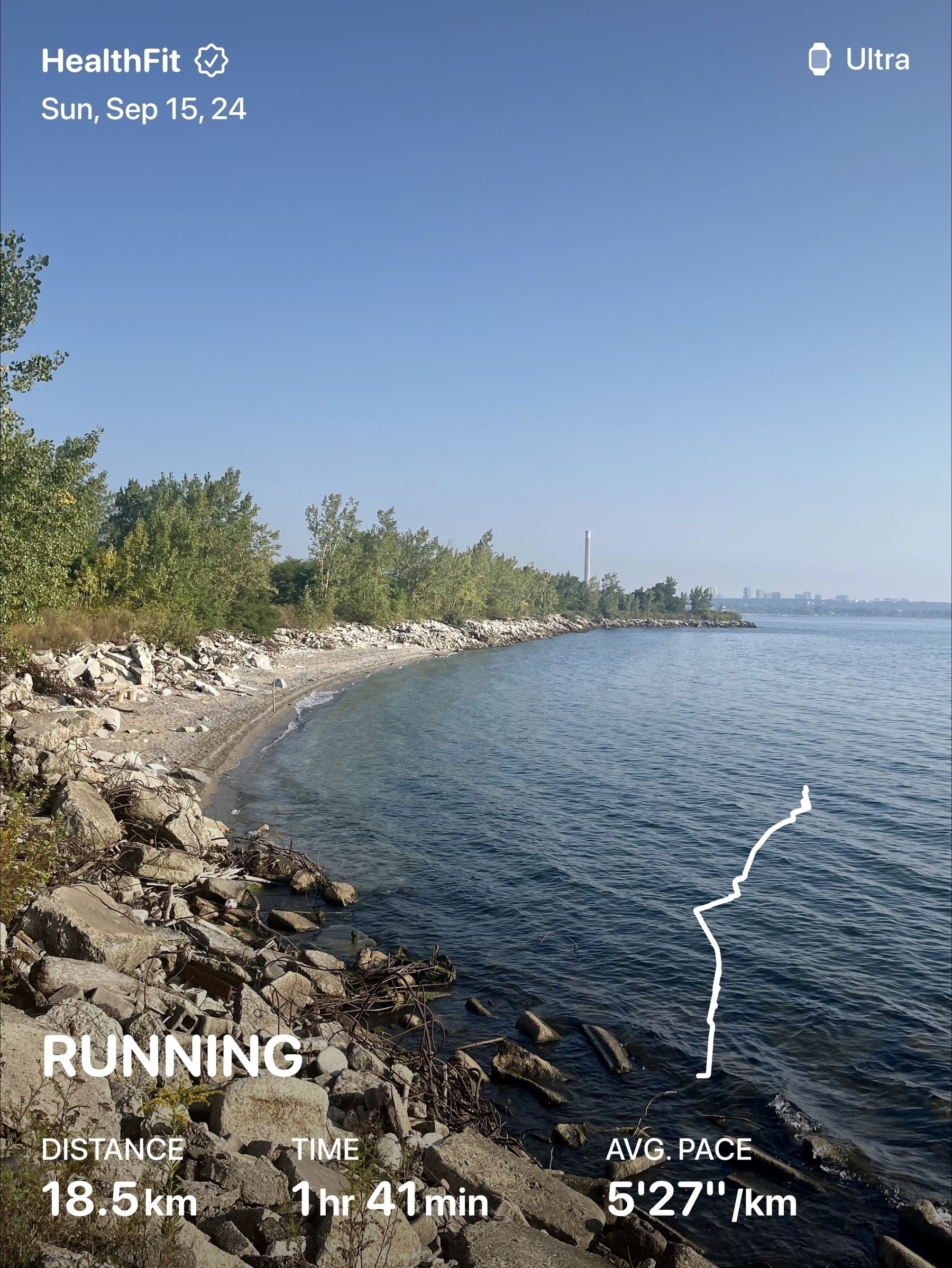 A scenic waterfront area features a rocky shoreline and dense trees, with a fitness app overlay displaying running statistics.