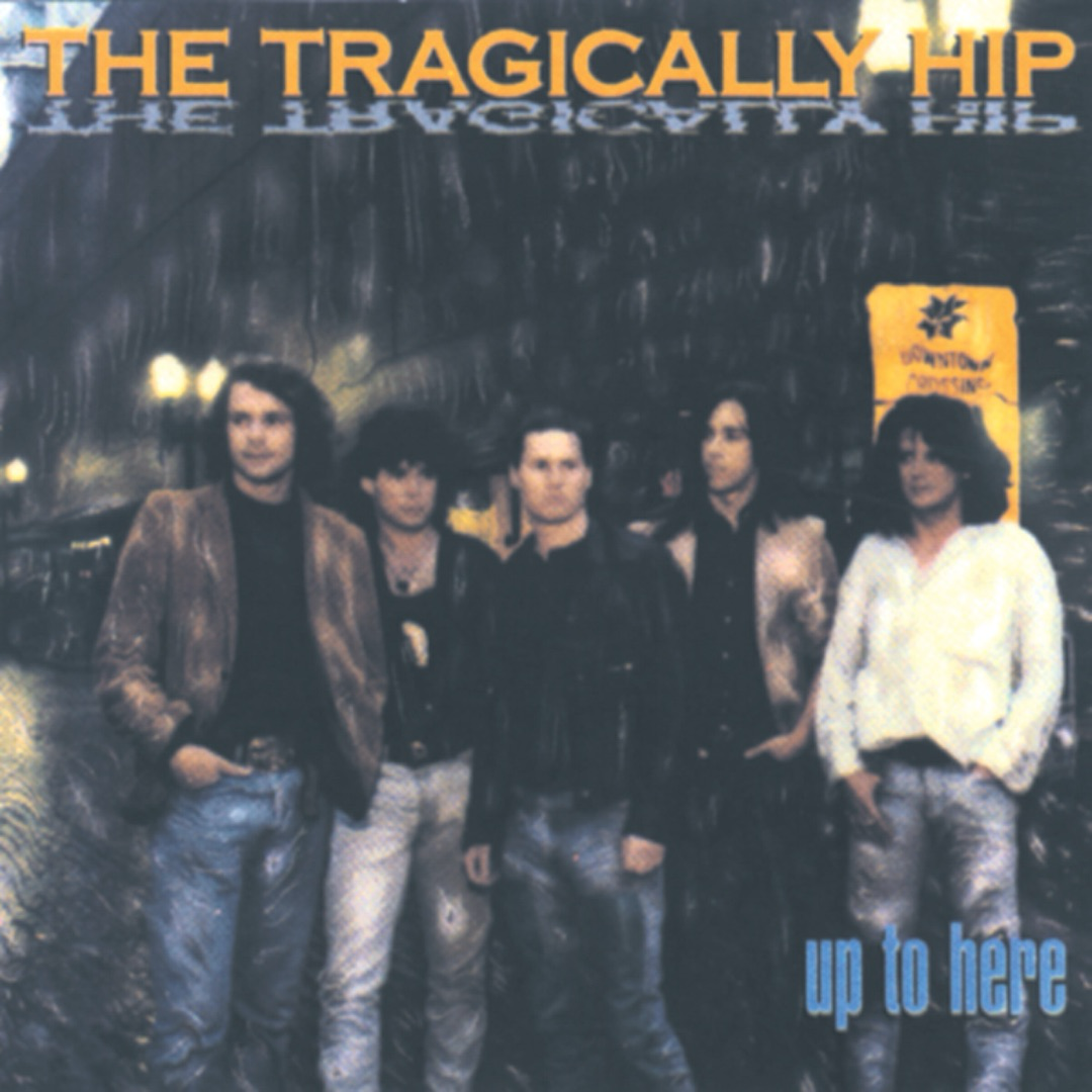 Auto-generated description: Five men stand together in front of a blurred, rainy street backdrop with the text THE TRAGICALLY HIP above them and up to here below.