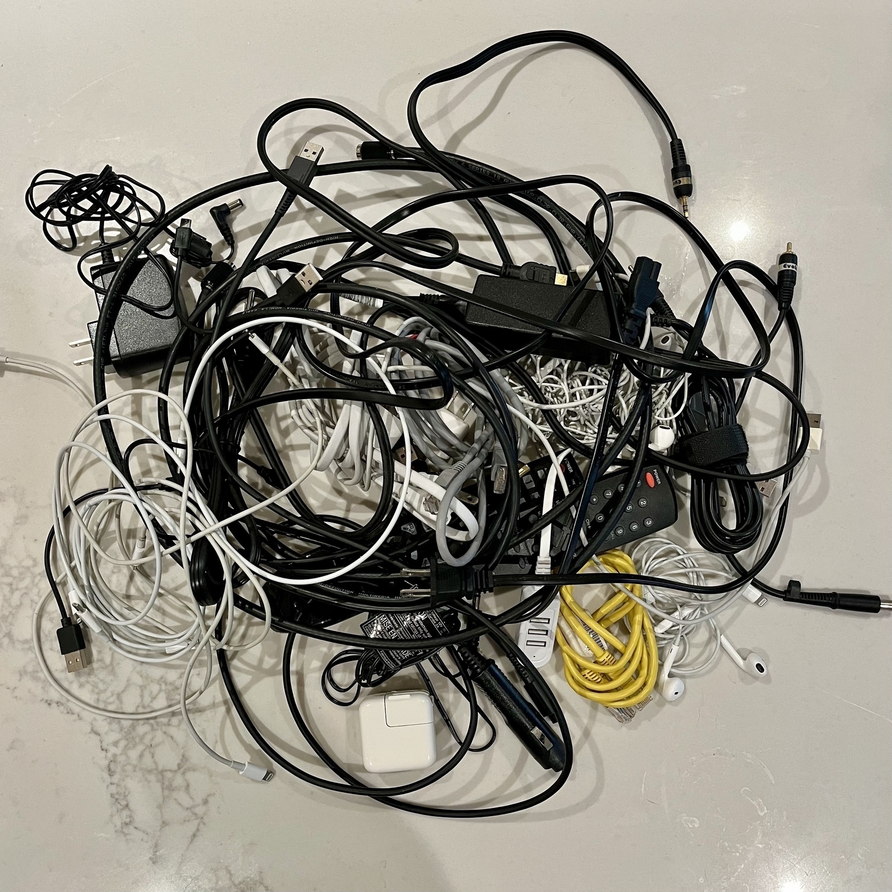 A tangled pile of various electronic cables and chargers is spread out on a surface.