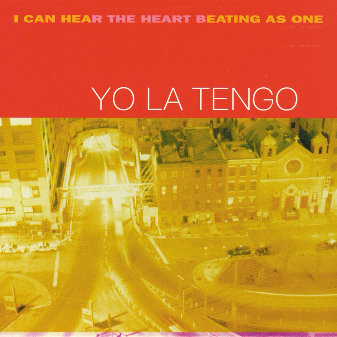 Auto-generated description: A vibrant, cityscape scene with yellow hues features prominently on the cover of Yo La Tengo's album I Can Hear the Heart Beating as One.