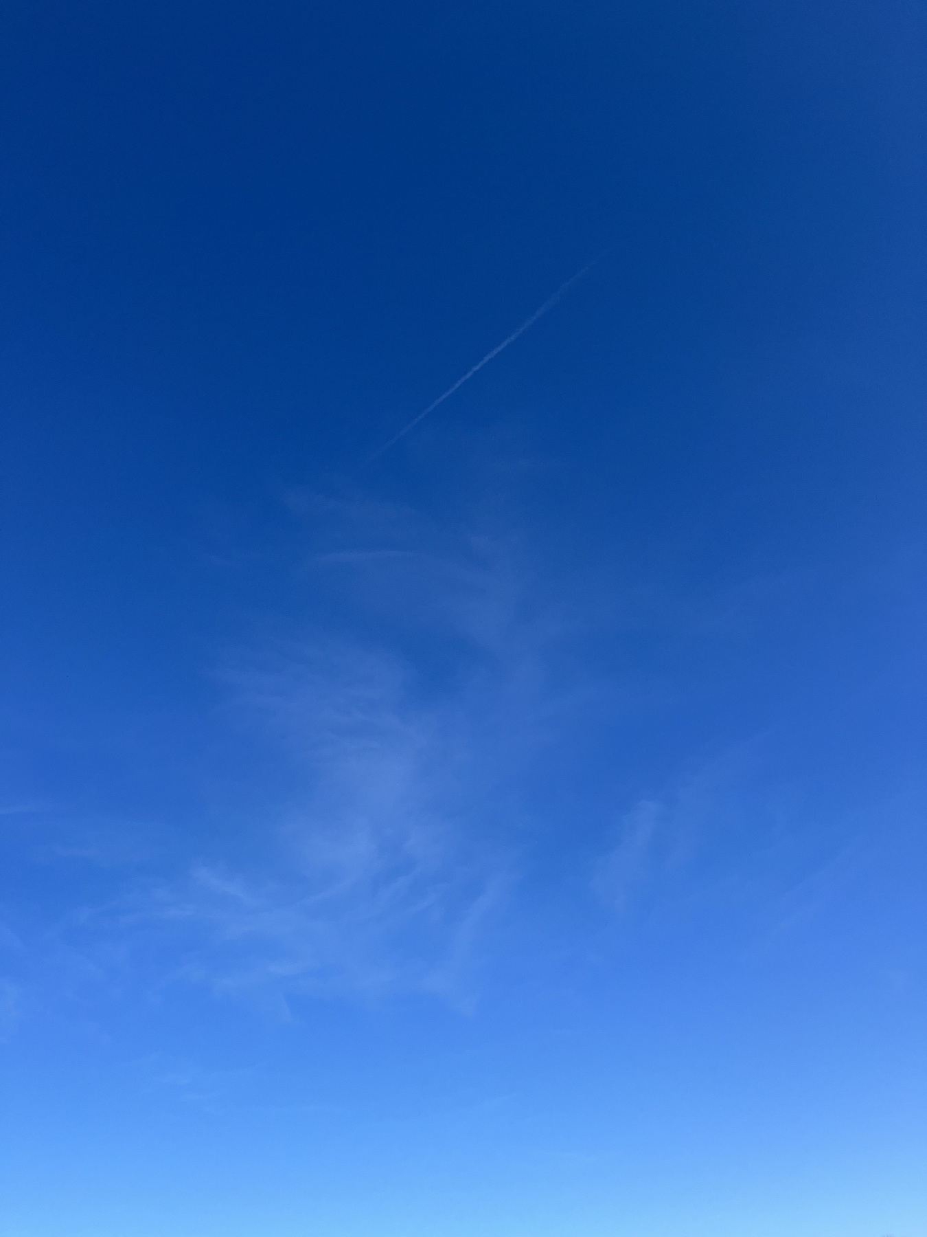 Clear blue sky with a single, slender contrail is present amidst faint wisps of clouds.