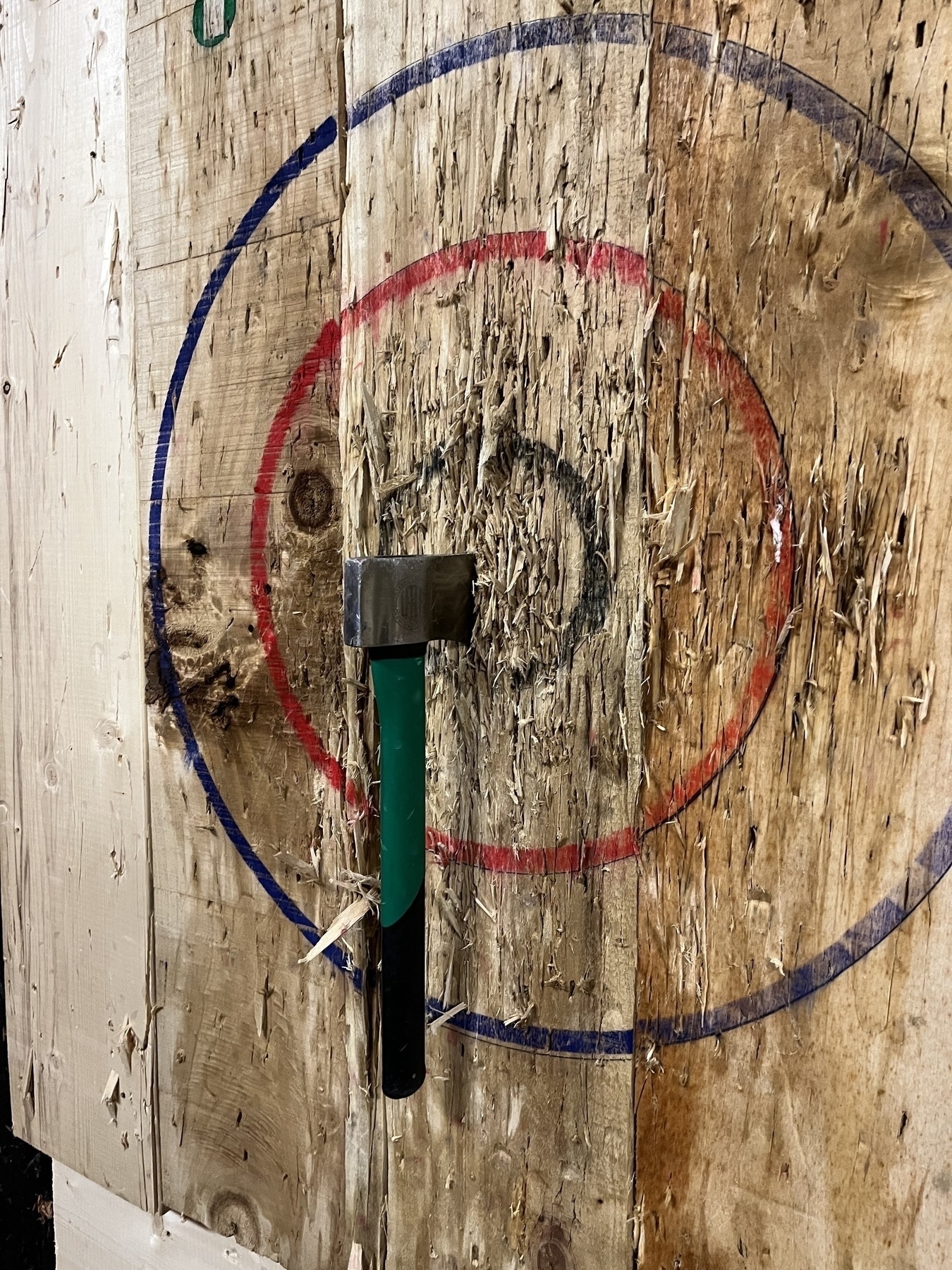 An axe is embedded in a wooden target with colored rings.