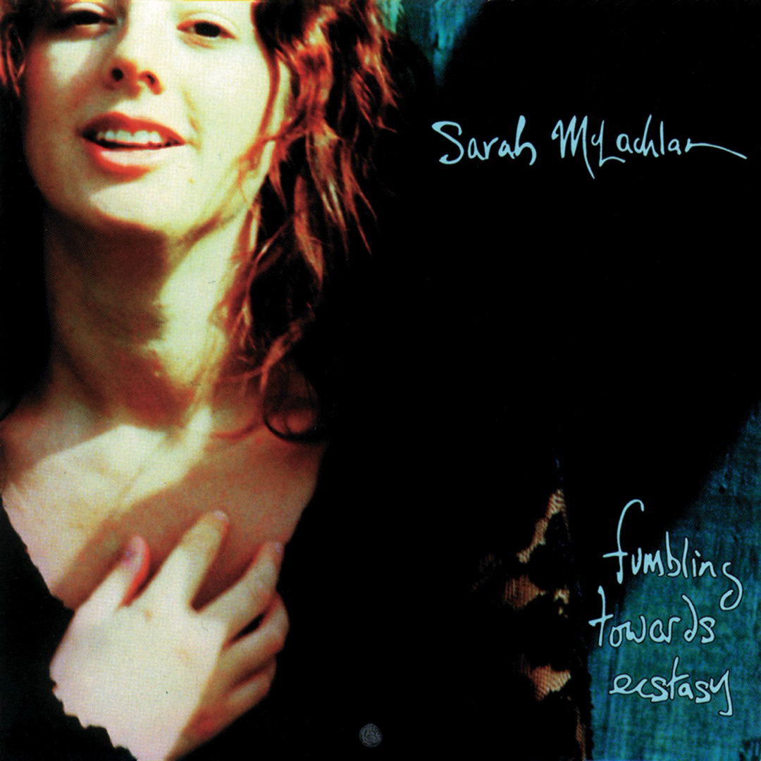 Auto-generated description: A woman with her hand on her chest is smiling in front of a dark background with the text Sarah McLachlan and fumbling towards ecstasy.