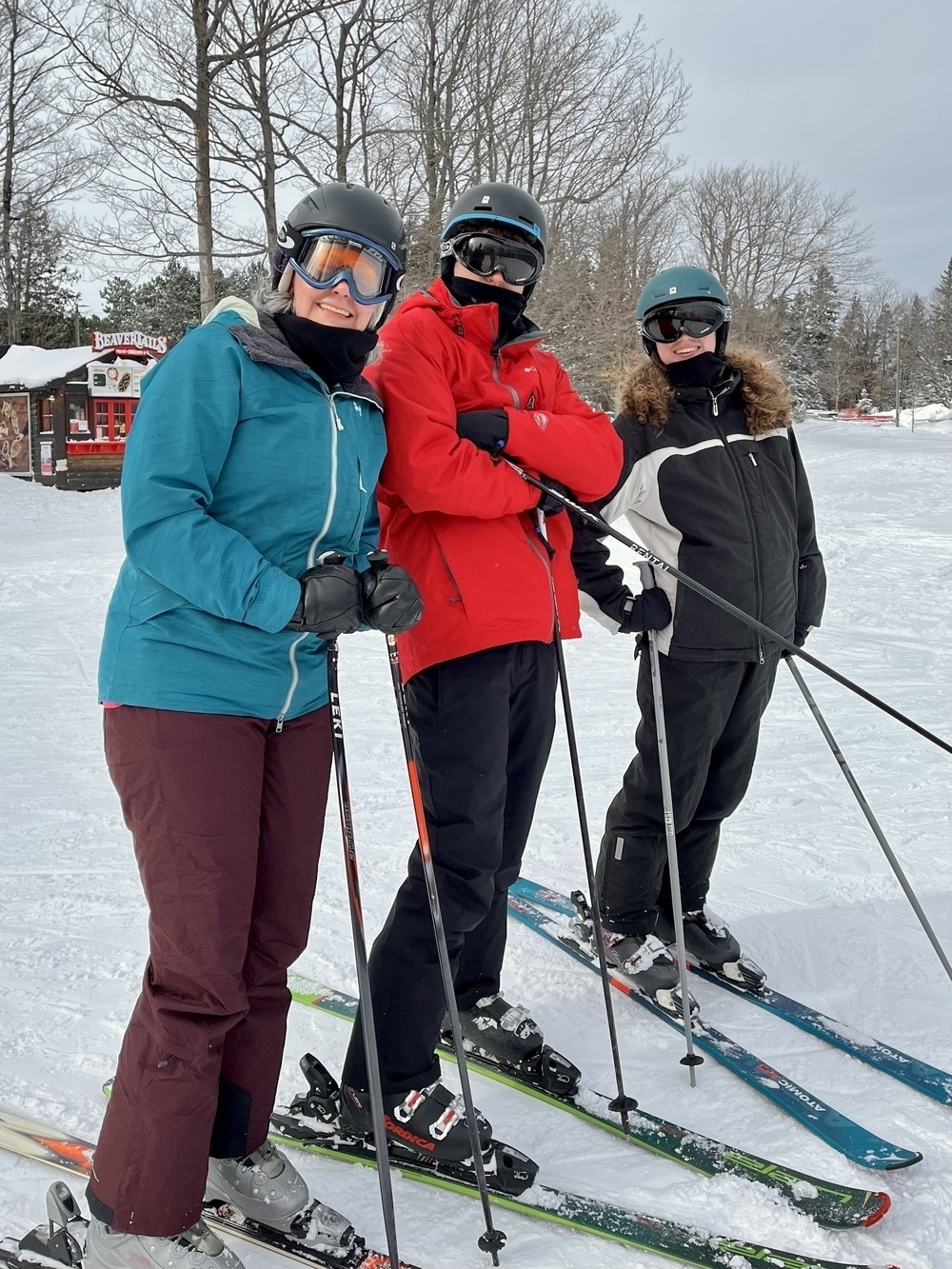 Three people in ski gear are posing together on a snowy slope with trees in the background.