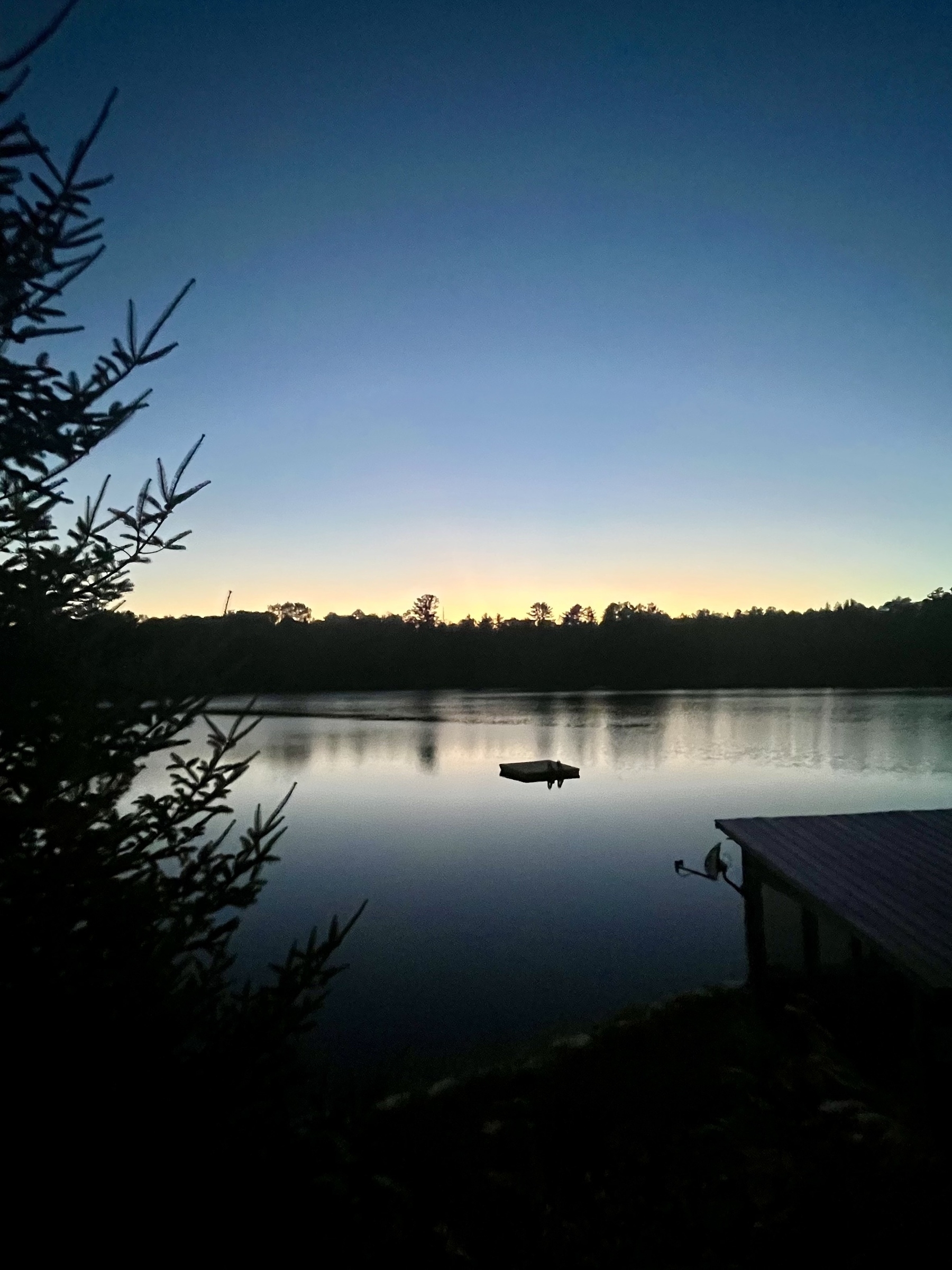 A tranquil lake scene at dusk features a silhouetted boat on the calm water, with trees and a dock in the foreground.