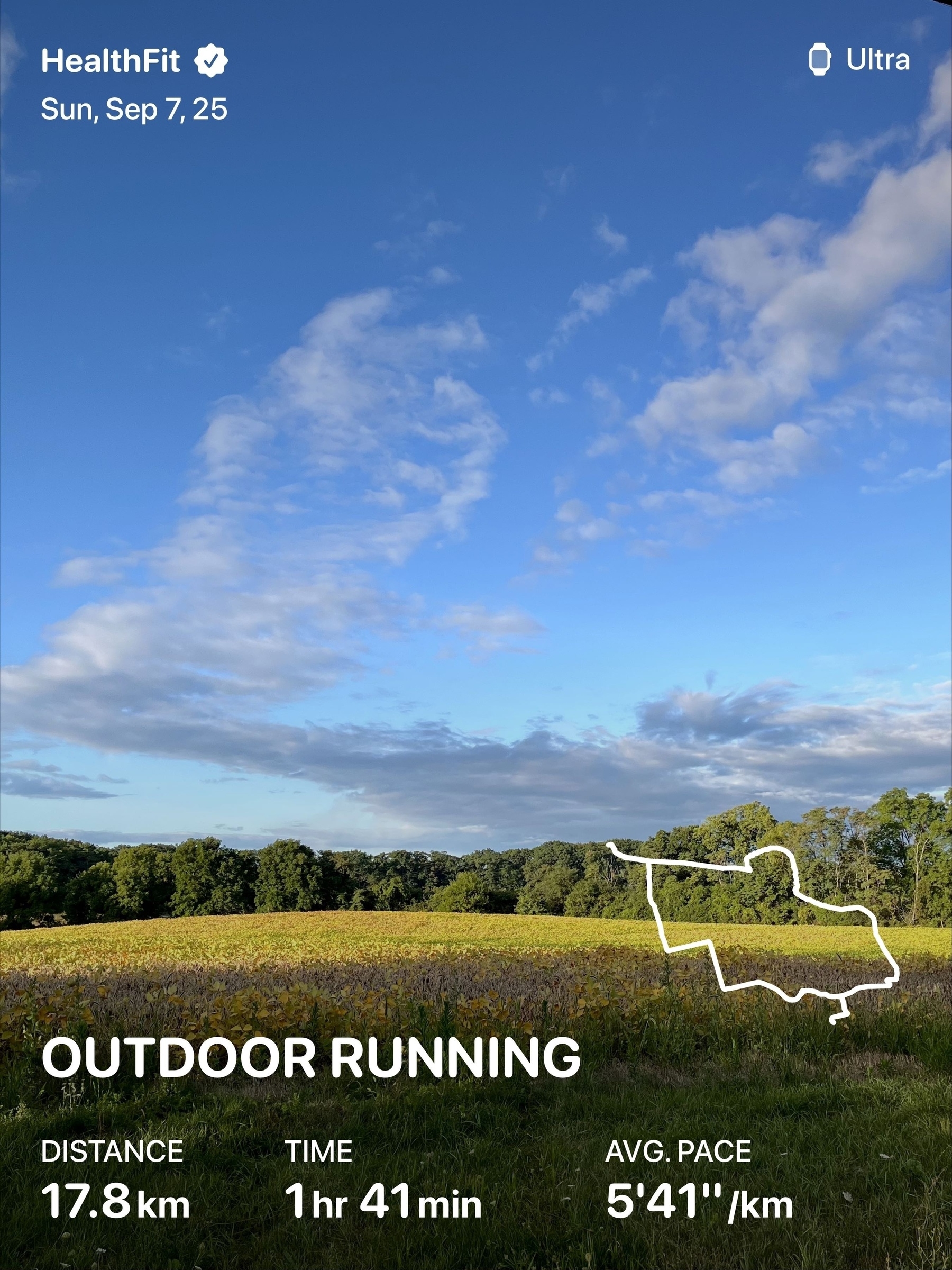 A serene landscape of a grassy field with trees under a partly cloudy sky is overlaid with data from a running app, showing details of a workout.