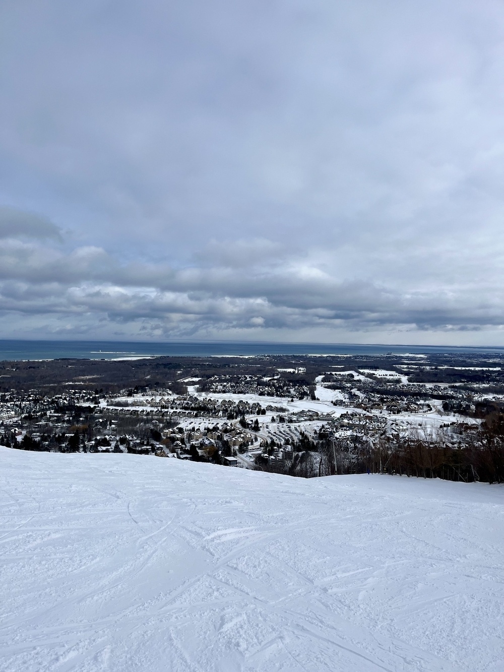 A snowy landscape overlooks a town with expansive cloudy skies above.