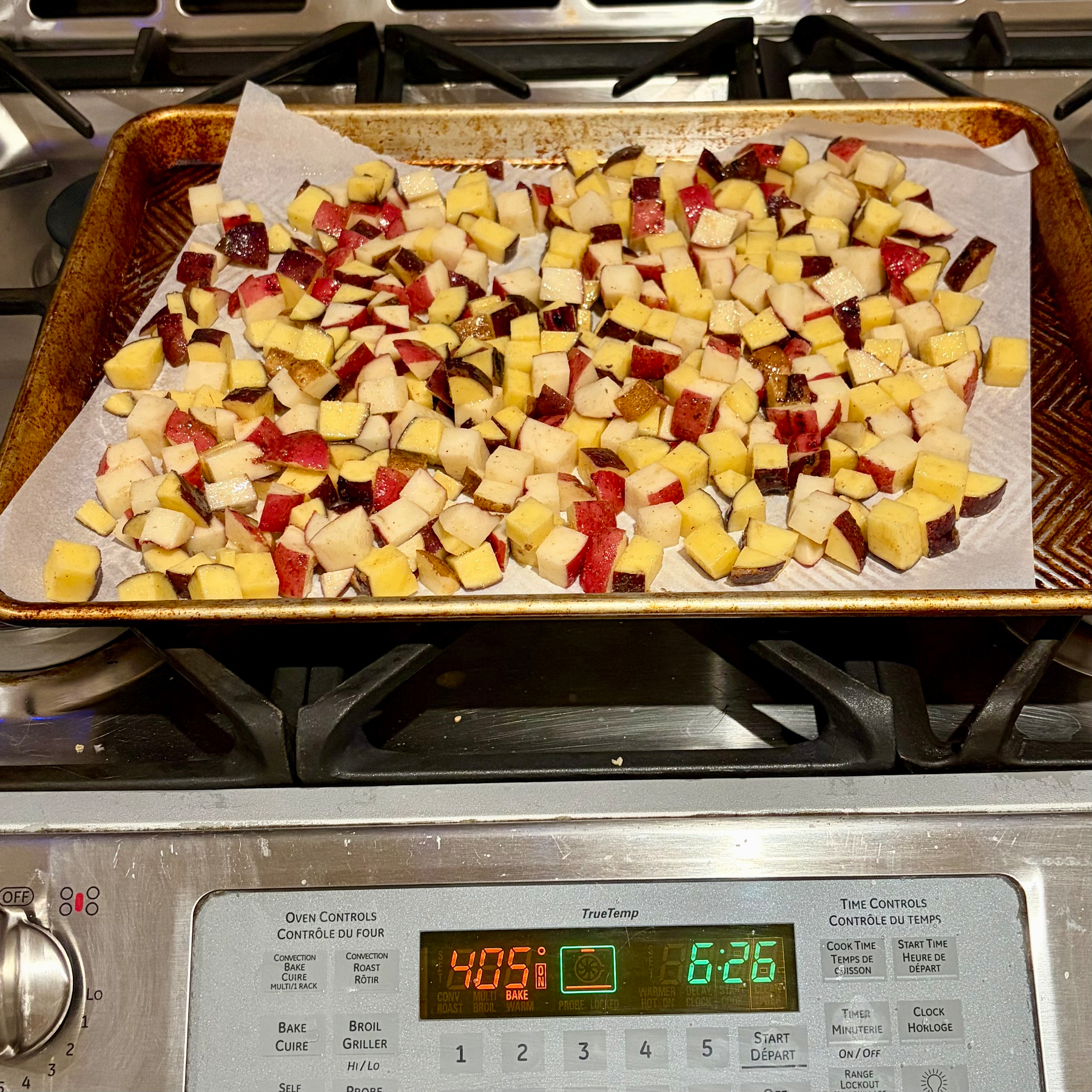 Diced potatoes are spread on a baking sheet lined with parchment paper, placed on a stovetop above an oven set to 400°F.