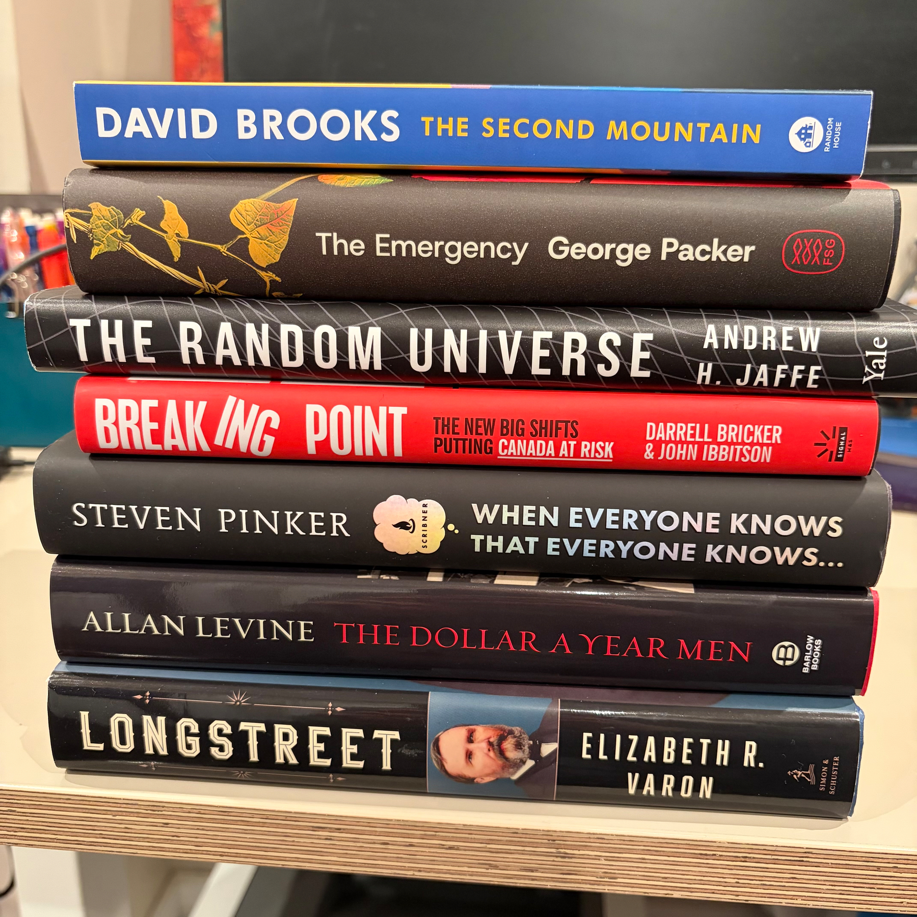 A stack of seven books with various titles and authors is displayed on a reflective surface.