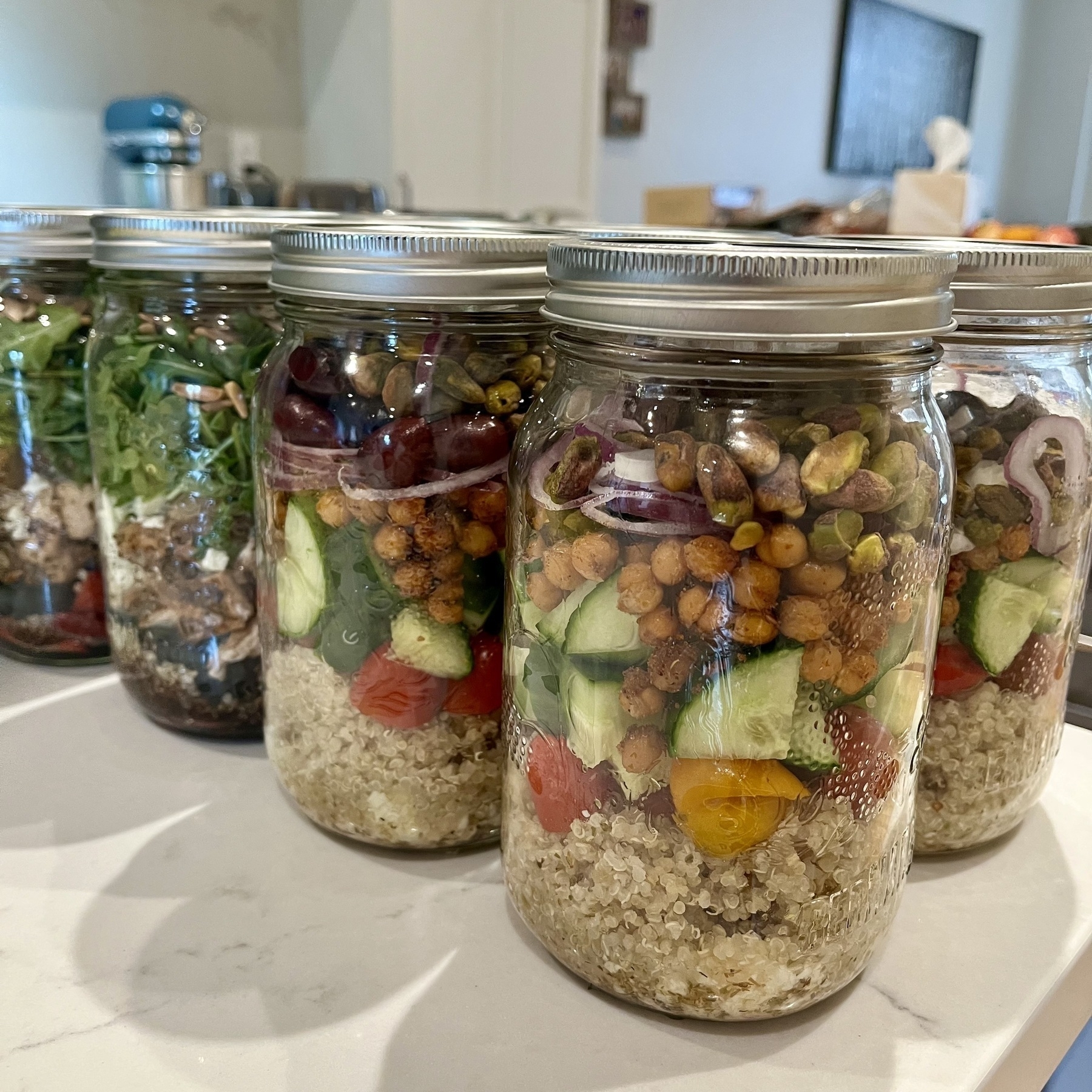 Several mason jars filled with salad ingredients arranged on a counter