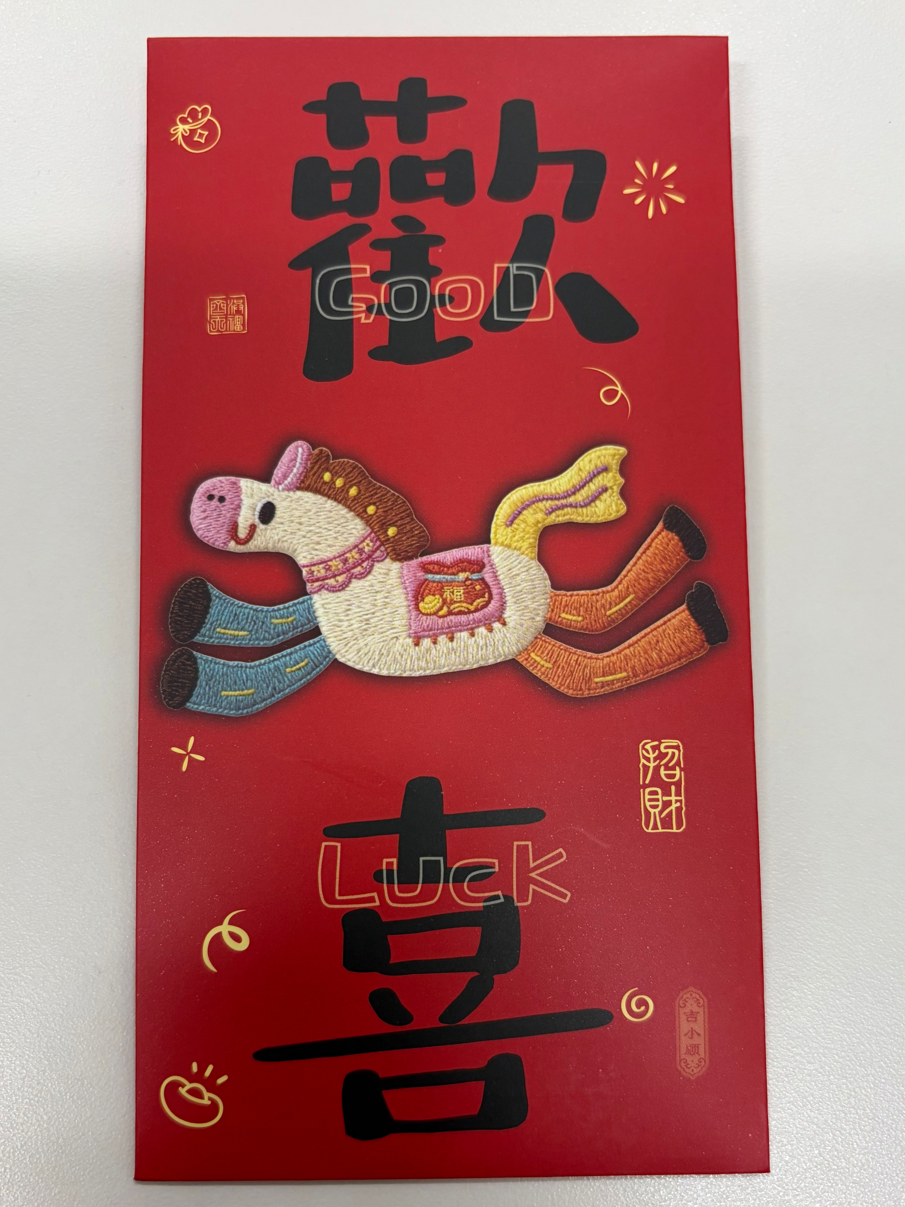 A red envelope decorated with colorful embroidery of a horse and Chinese characters associated with good fortune and happiness.