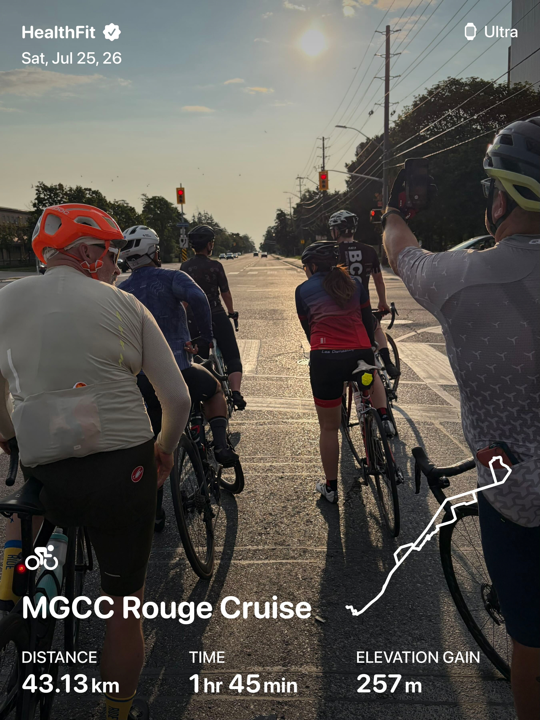 A group of cyclists is stopped at a red light on a sunny road, preparing to continue their ride.