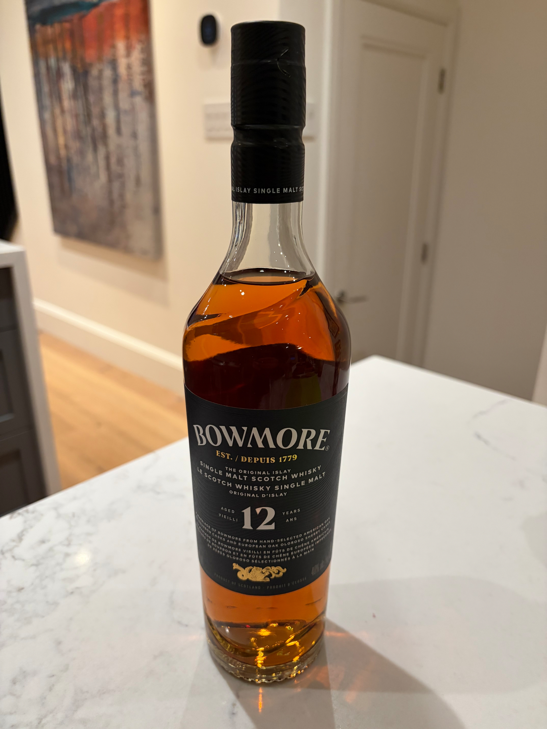 A bottle of Bowmore 12-year single malt Scotch whisky is placed on a white countertop in a modern interior setting.