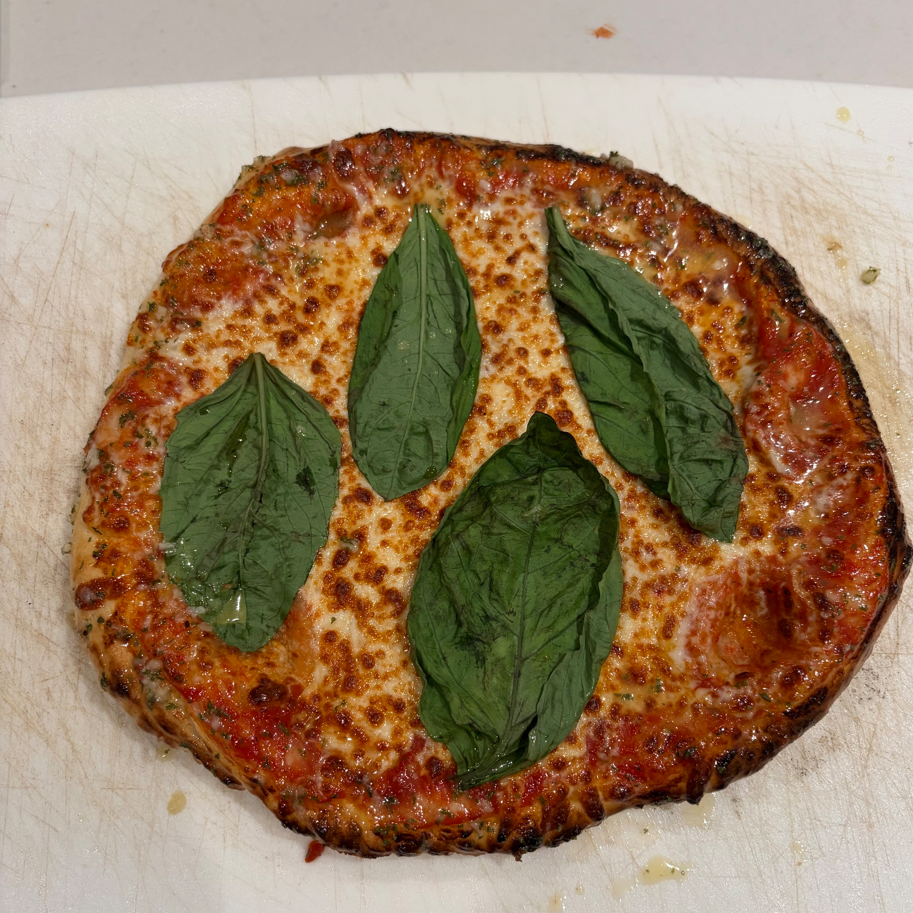 A cooked pizza topped with fresh basil leaves sits on a surface.