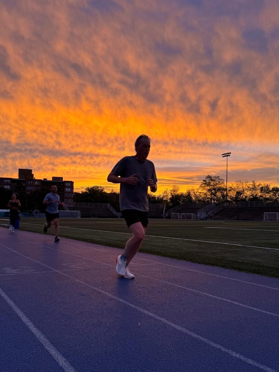 Several people are running on a track during a vibrant orange and purple sunset.