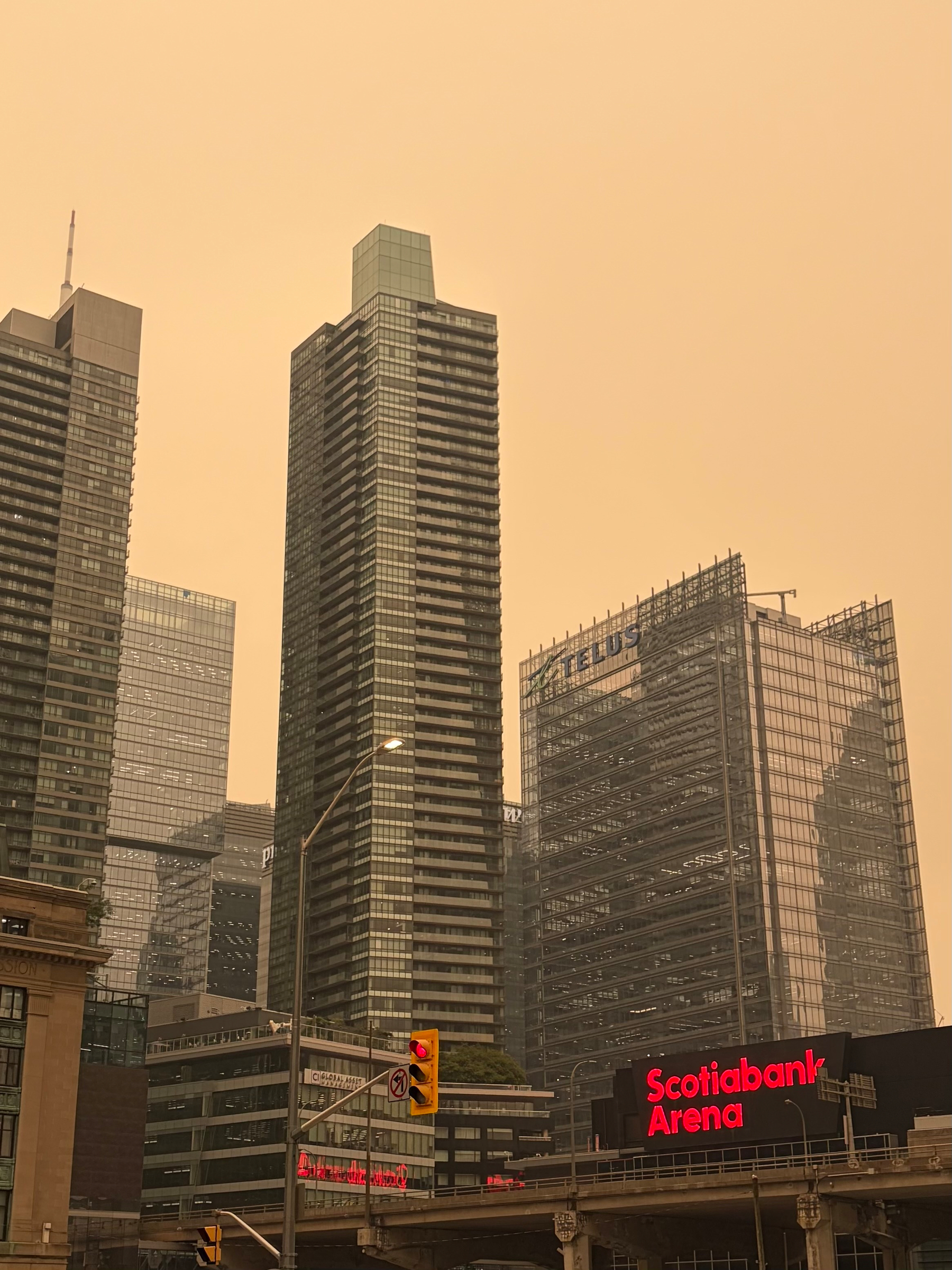 Tall skyscrapers with prominent signs for Scotiabank Arena and TELUS stand under an orange-tinted sky, likely due to atmospheric conditions.