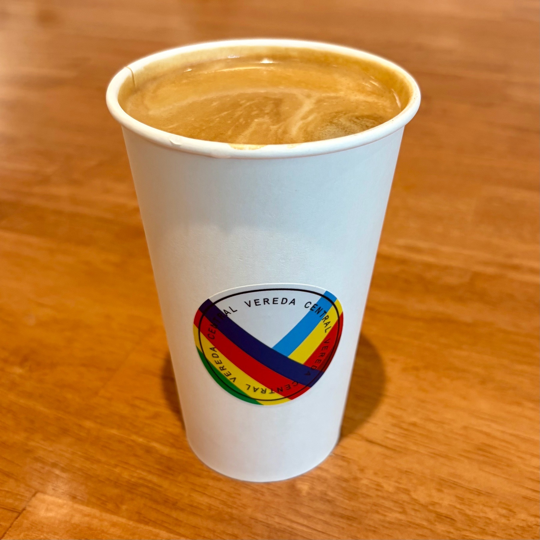 An Americano coffee on a wood table with a colourful Vereda Central sticker