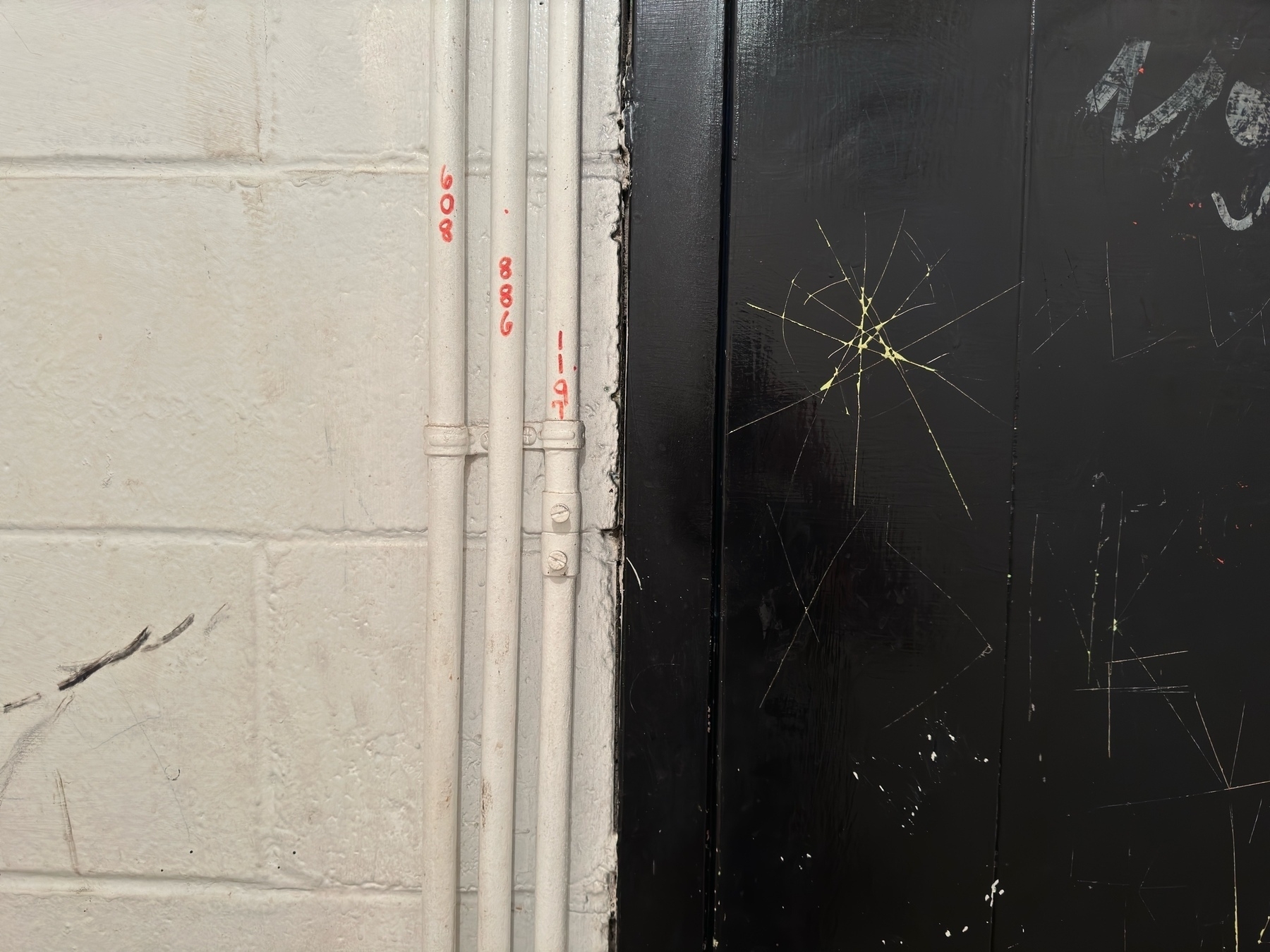 a dark brown graffiti-covered door next to an off-white wall with exposed conduit. Industrial theming.