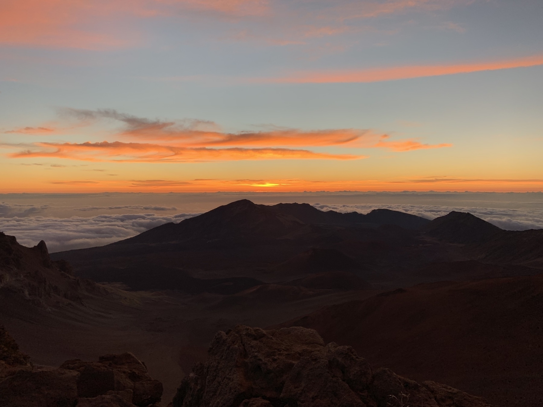 Photo of a sunrise over clouds and a barren volcanic landscape