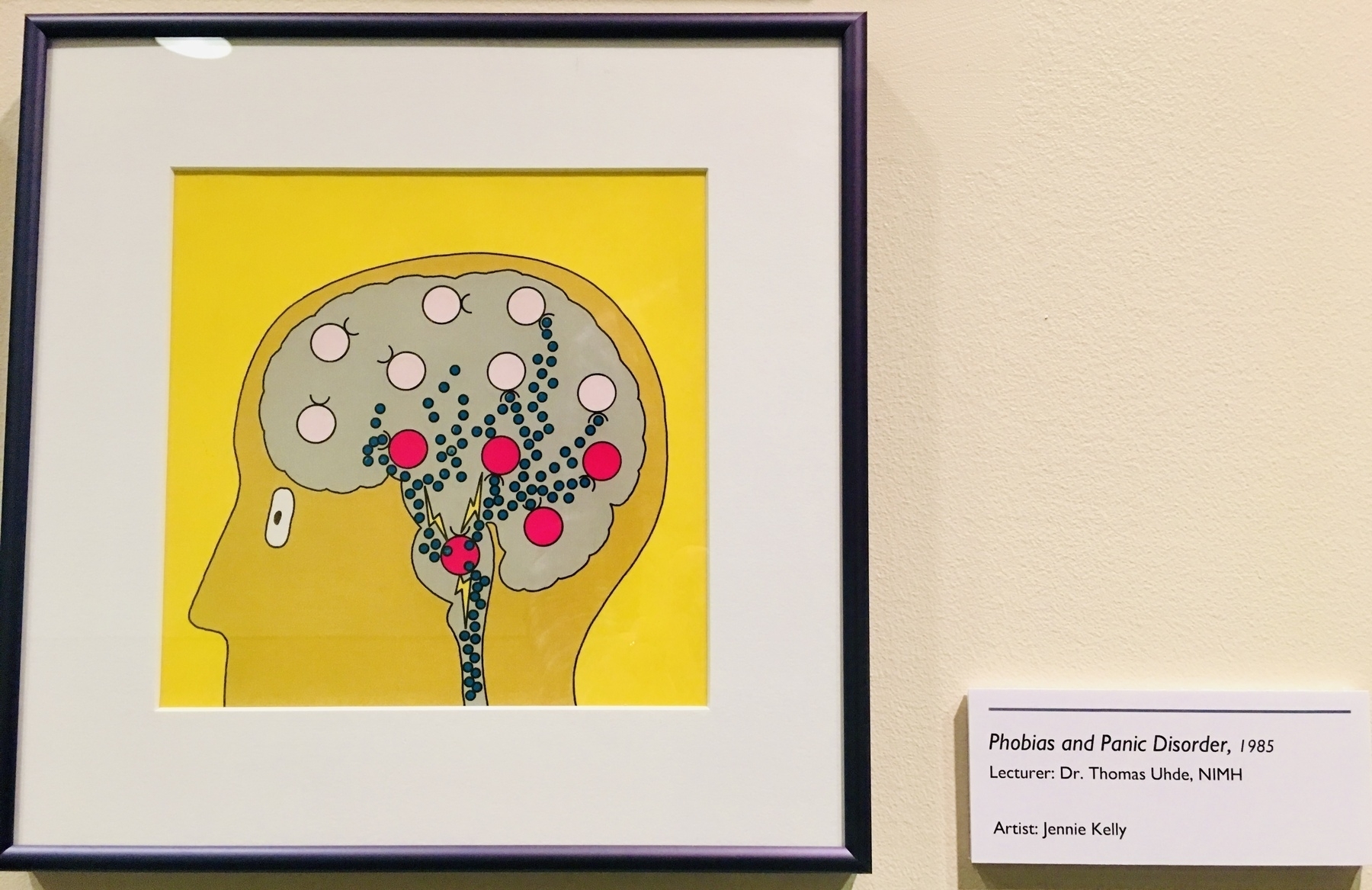 Photo of a framed cartoon drawing showing  a human profile with an overlayed brain covered in pale pink and red circles connected by green dots.