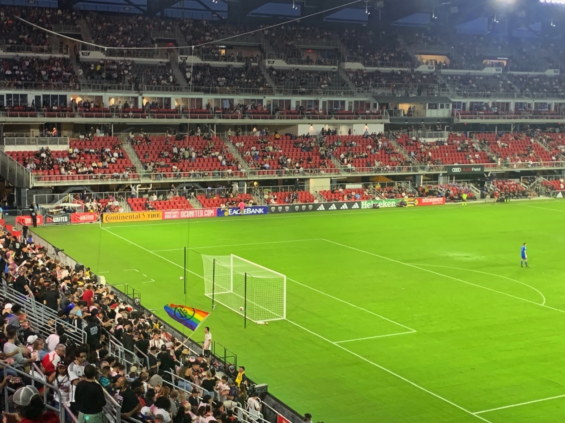 Audi Field (DC United’s stadium) during a game with Montreal. The seats are half-empty at the top, but packed on the left side, with one of the fans waiving a rainbow flag.