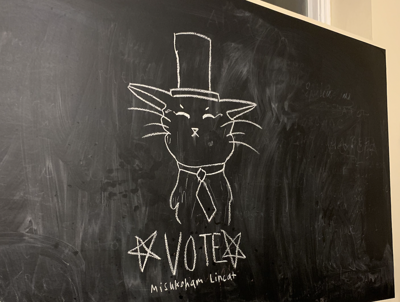 A chalk drawing of a cat wearing a top hat and a tie, facing the viewer. *VOTE* is written below in large letters, “Mishkoham Lincat” in smaller letters below. 