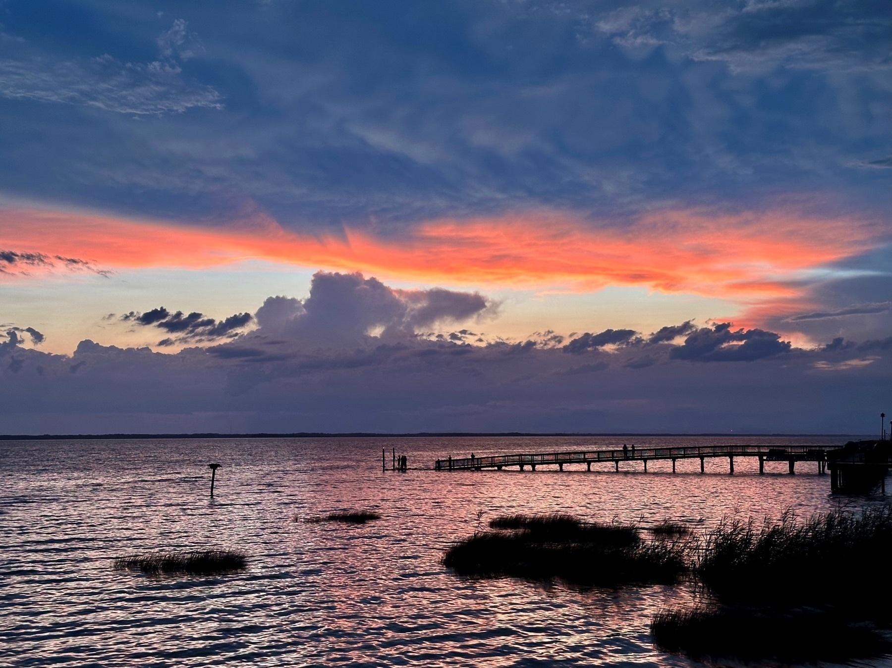 Duck, Nort Carolina, at sunset. The photo is centered on 3 tiny silhouettes perched on a fishing platform at the end of a boardwalk.