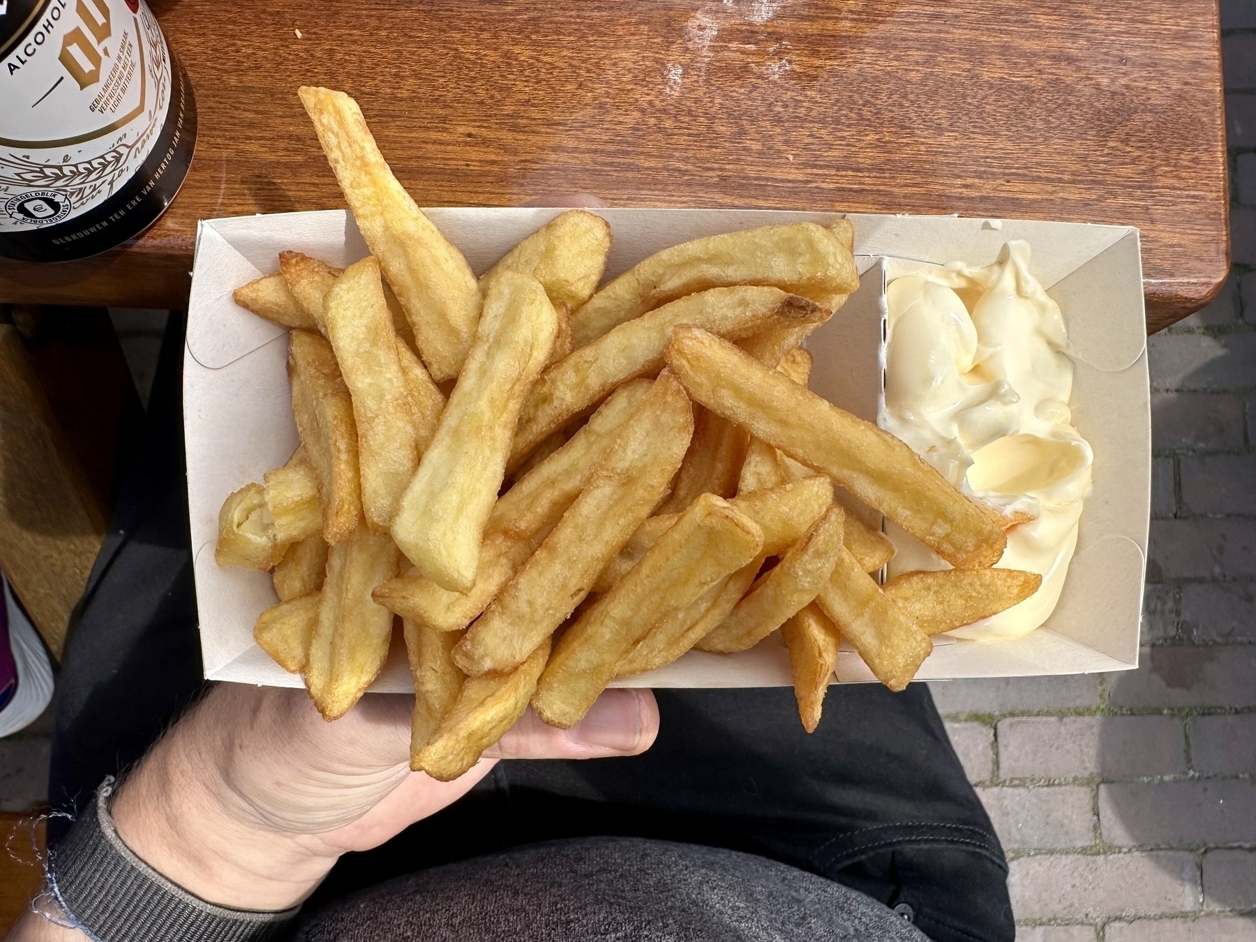A person is holding a cardboard tray filled with golden fries and a side of mayonnaise.