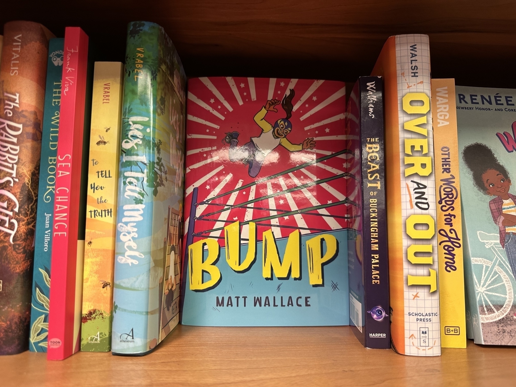 Photo of a bookshelf with the book Bump by Matt Wallace facing forward, a girl luchador on the cover.